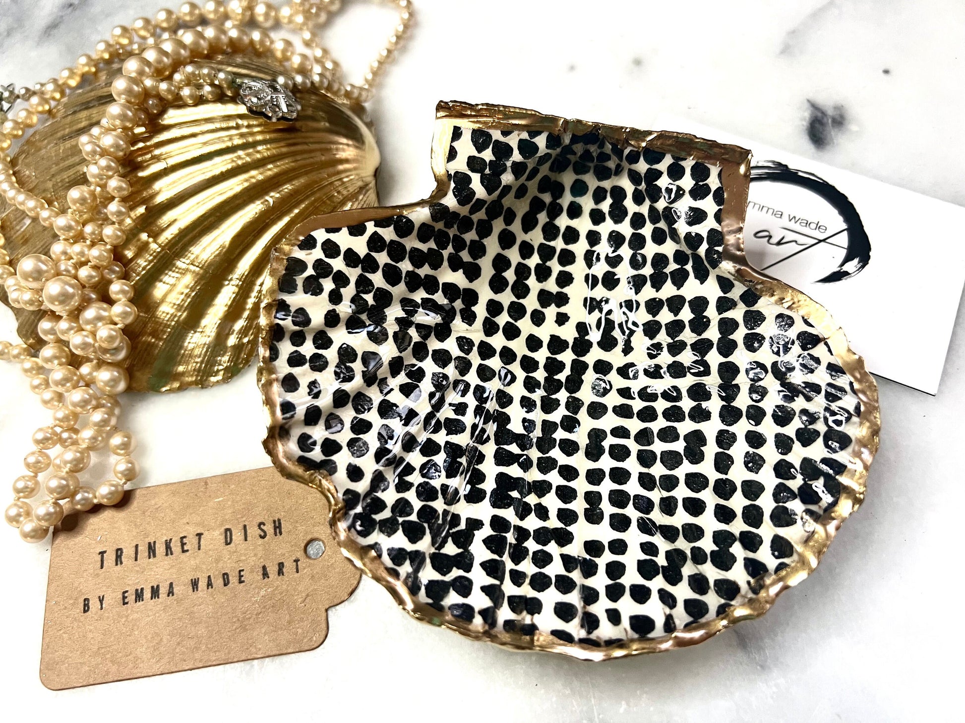 Handcrafted black and white dotted Dorset scallop shell trinket dish, gilded with real gold leaf and sealed in crystal-clear resin. Perfect as a jewellery holder, cufflink tray, tea light holder, or coastal home accent. Each eco-friendly shell is ethically sourced from the Dorset coastline, individually hand finished in Surrey, and presented in a sustainable gift box. A thoughtful handmade gift for ocean lovers, weddings, birthdays, or coastal home décor.