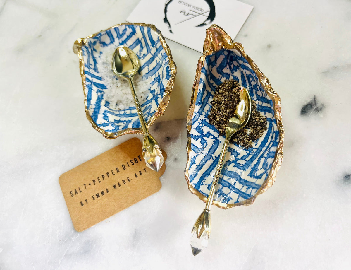 Handmade blue fretwork oyster shell salt and pepper pinch pots shown as a matching pair with small gold spoons, crafted from natural Dorset oyster shells. Each shell features a striking blue fretwork maze pattern, sealed with crystal-clear food-safe resin and finished with shimmering gold leaf edges. Coastal-inspired shell cruet dishes, perfect for table decor, weddings, or a unique luxury hostess gift, with each piece one of a kind.