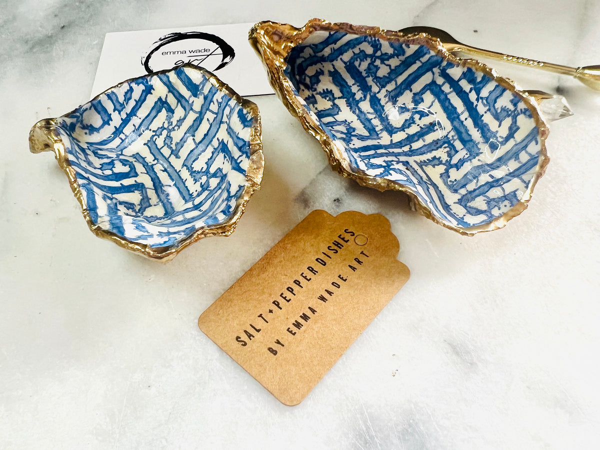 Handmade blue fretwork oyster shell salt and pepper pinch pots shown as a matching pair with small gold spoons, crafted from natural Dorset oyster shells. Each shell features a striking blue fretwork maze pattern, sealed with crystal-clear food-safe resin and finished with shimmering gold leaf edges. Coastal-inspired shell cruet dishes, perfect for table decor, weddings, or a unique luxury hostess gift, with each piece one of a kind.