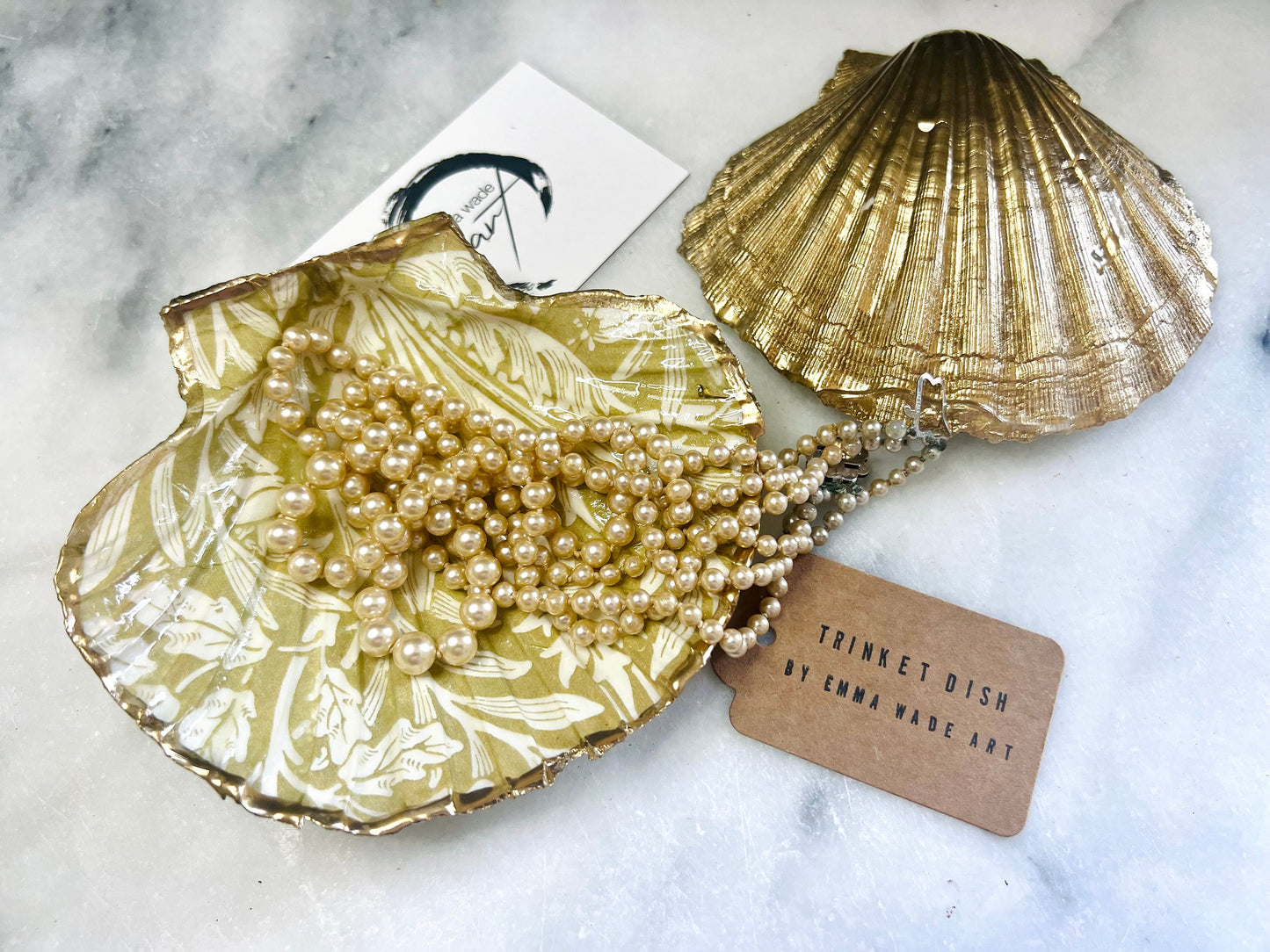 Handmade scallop shell trinket dishes featuring a William Morris gold and ivory acorn heritage pattern with shimmering liquid gold leaf edging. Natural Dorset scallop shells sealed in glossy crystal clear resin and styled as luxury jewellery holders, vanity trays and coastal home décor accessories. Elegant Arts and Crafts inspired shell dishes photographed on a marble background with pearls and decorative styling.