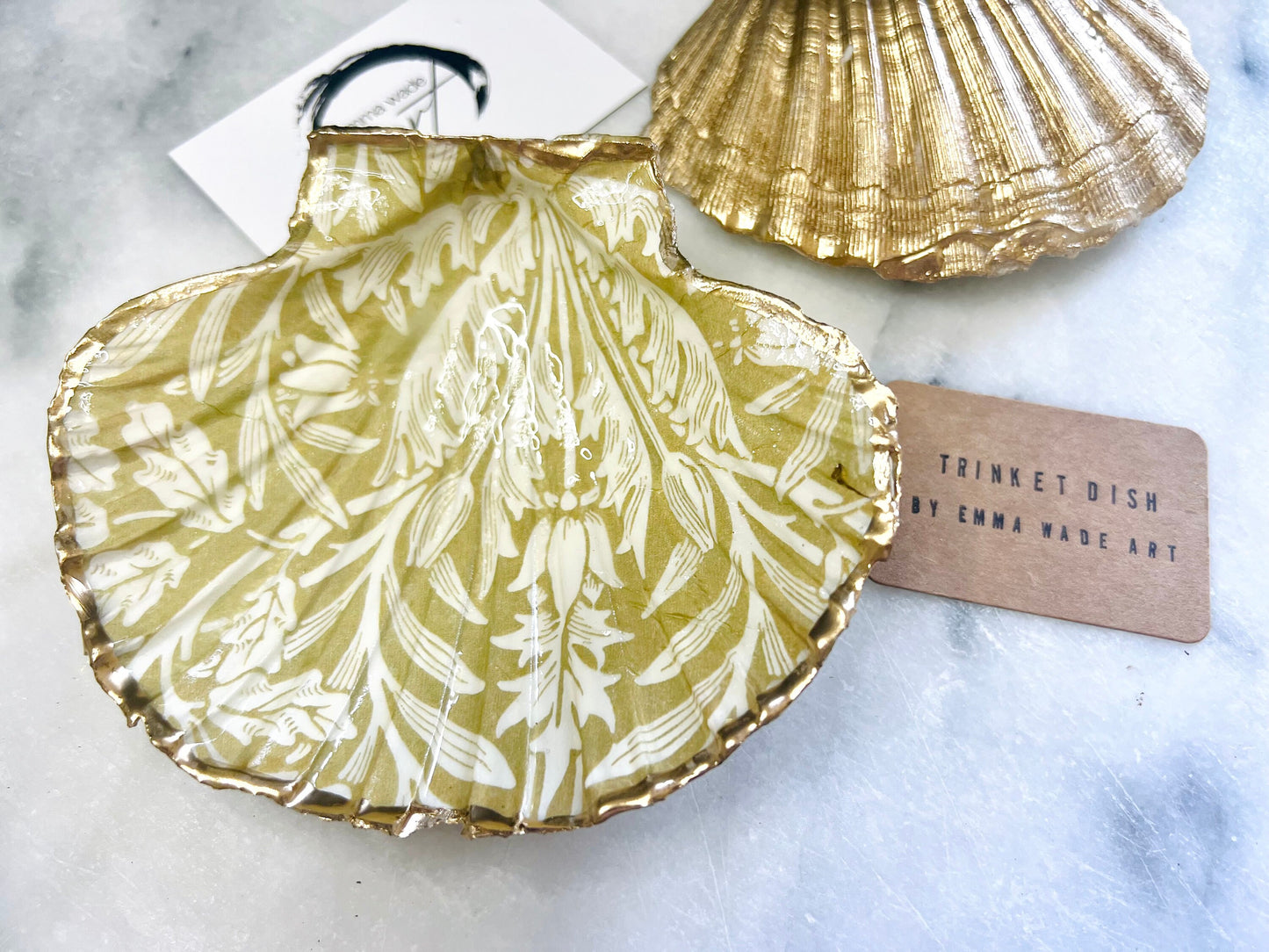 Handmade scallop shell trinket dishes featuring a William Morris gold and ivory acorn heritage pattern with shimmering liquid gold leaf edging. Natural Dorset scallop shells sealed in glossy crystal clear resin and styled as luxury jewellery holders, vanity trays and coastal home décor accessories. Elegant Arts and Crafts inspired shell dishes photographed on a marble background with pearls and decorative styling.