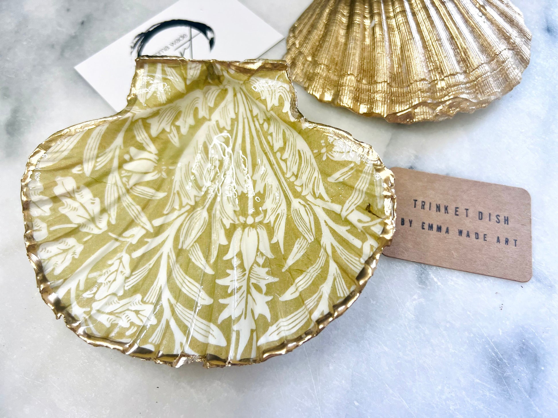 Handmade scallop shell trinket dishes featuring a William Morris gold and ivory acorn heritage pattern with shimmering liquid gold leaf edging. Natural Dorset scallop shells sealed in glossy crystal clear resin and styled as luxury jewellery holders, vanity trays and coastal home décor accessories. Elegant Arts and Crafts inspired shell dishes photographed on a marble background with pearls and decorative styling.