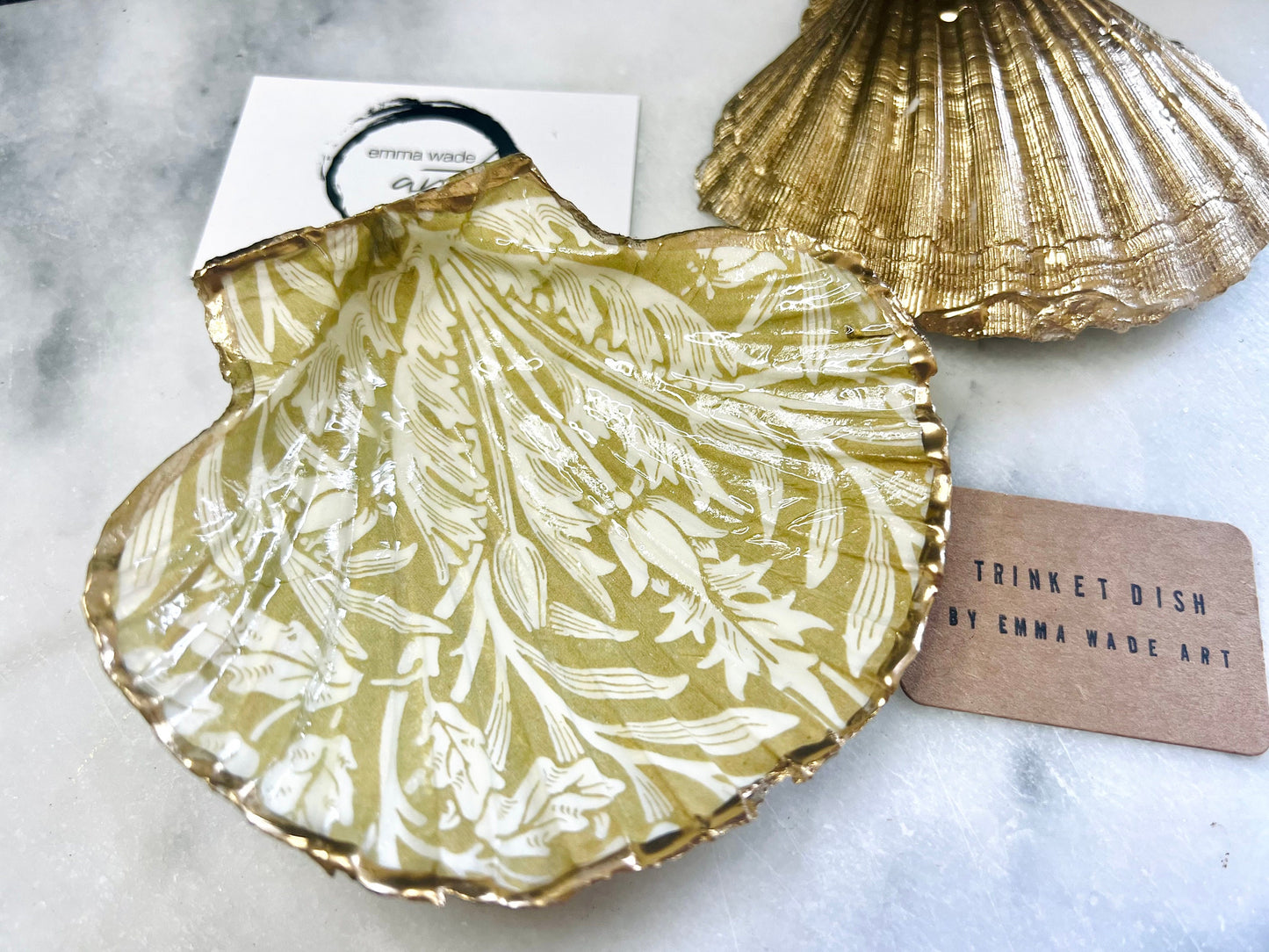 Handmade scallop shell trinket dishes featuring a William Morris gold and ivory acorn heritage pattern with shimmering liquid gold leaf edging. Natural Dorset scallop shells sealed in glossy crystal clear resin and styled as luxury jewellery holders, vanity trays and coastal home décor accessories. Elegant Arts and Crafts inspired shell dishes photographed on a marble background with pearls and decorative styling.