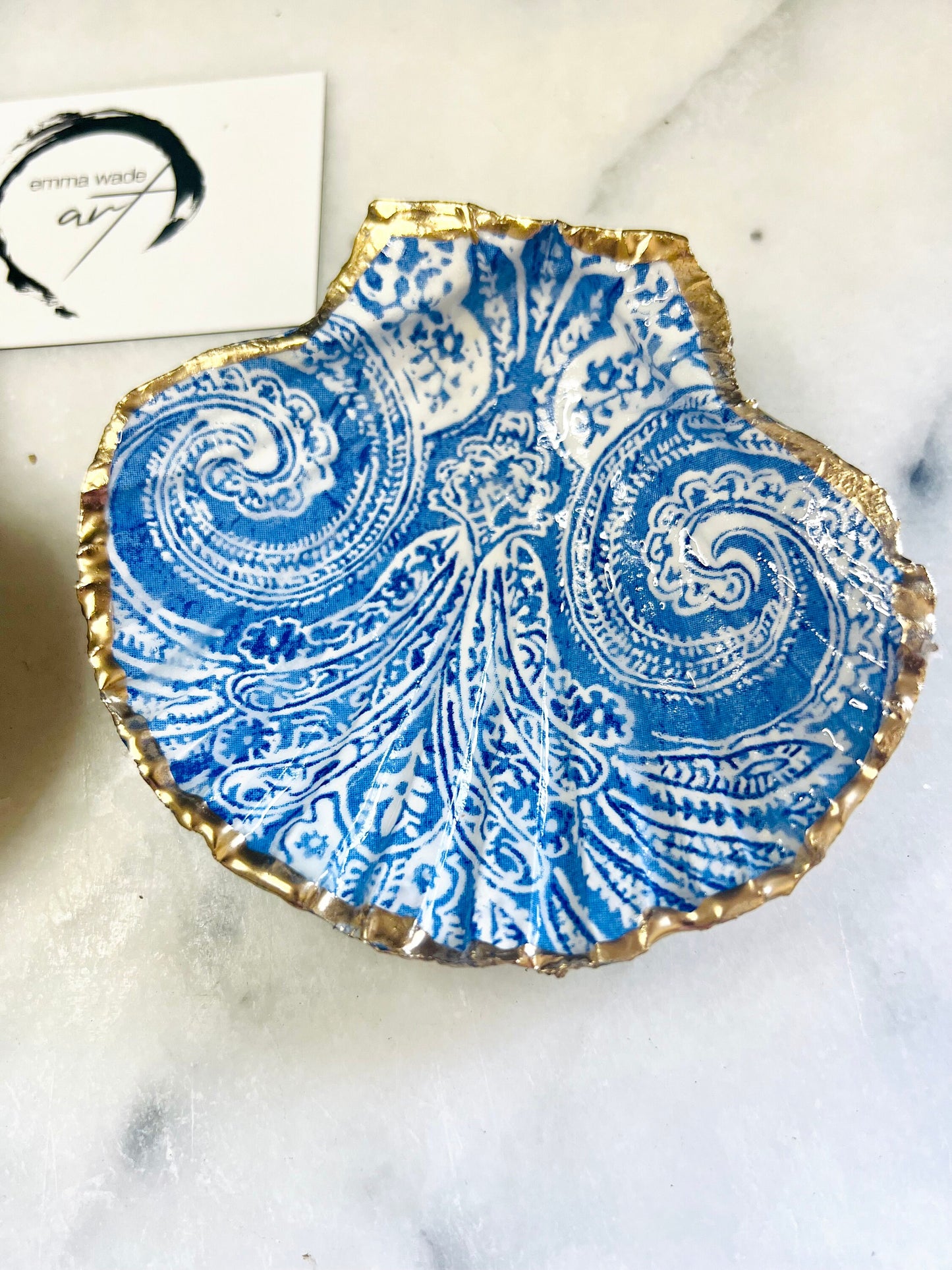 Blue and white paisley scallop shell ring catcher with hand applied gold leaf edging and glossy resin finish. Handmade Dorset shell jewellery tray styled with pearls on a marble background. Coastal vanity decor and luxury beach house accessory gift.