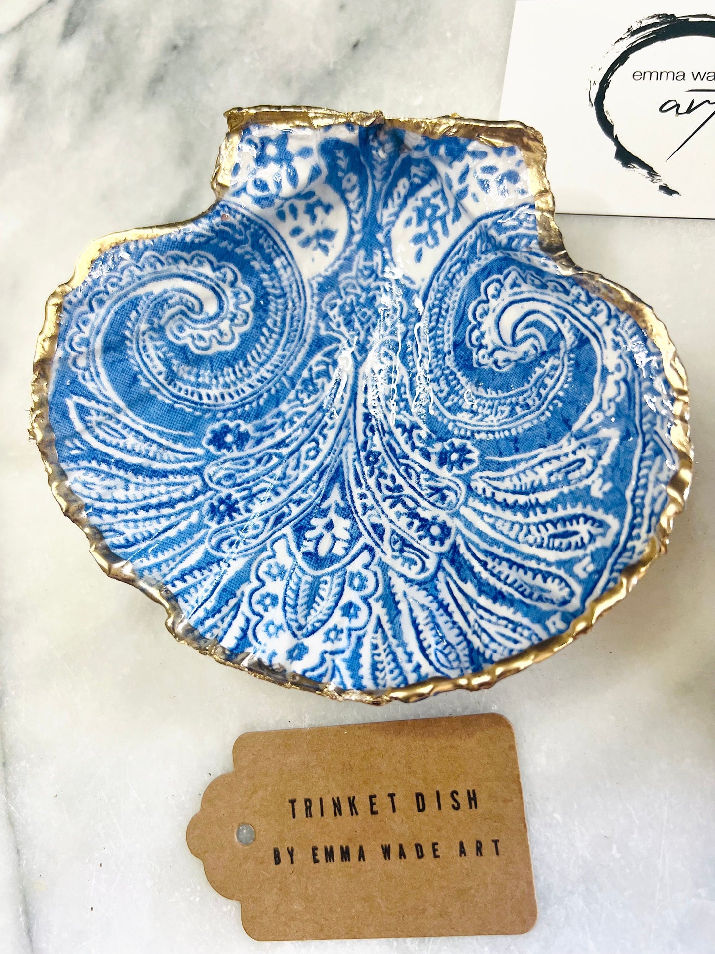 Blue and white paisley scallop shell ring catcher with hand applied gold leaf edging and glossy resin finish. Handmade Dorset shell jewellery tray styled with pearls on a marble background. Coastal vanity decor and luxury beach house accessory gift.