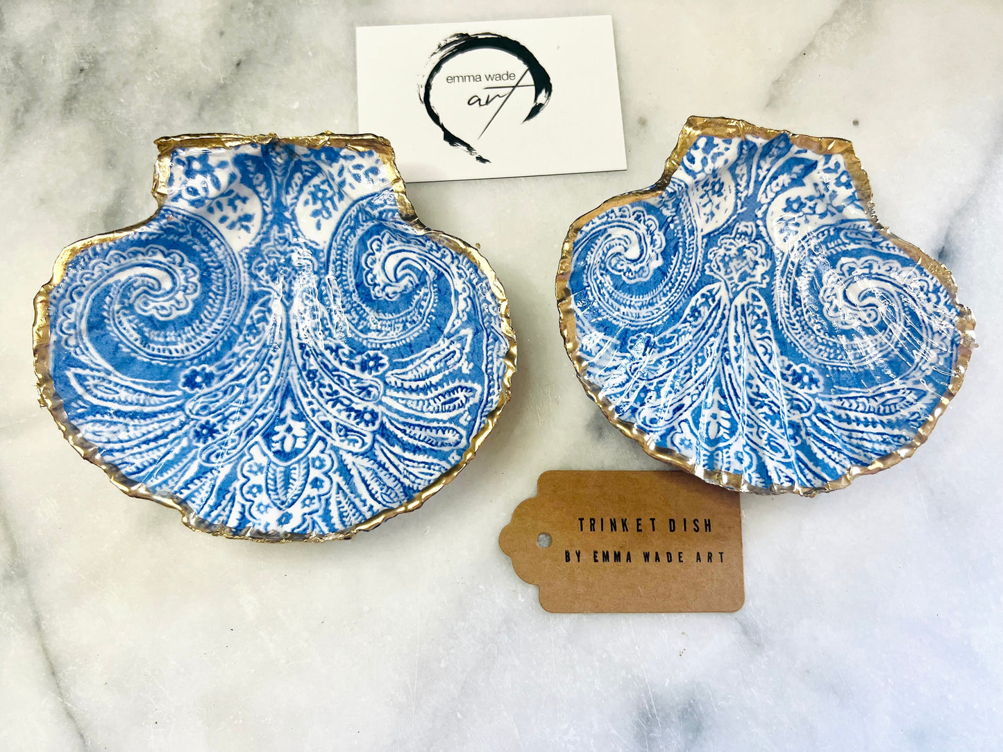Blue and white paisley scallop shell ring catcher with hand applied gold leaf edging and glossy resin finish. Handmade Dorset shell jewellery tray styled with pearls on a marble background. Coastal vanity decor and luxury beach house accessory gift.