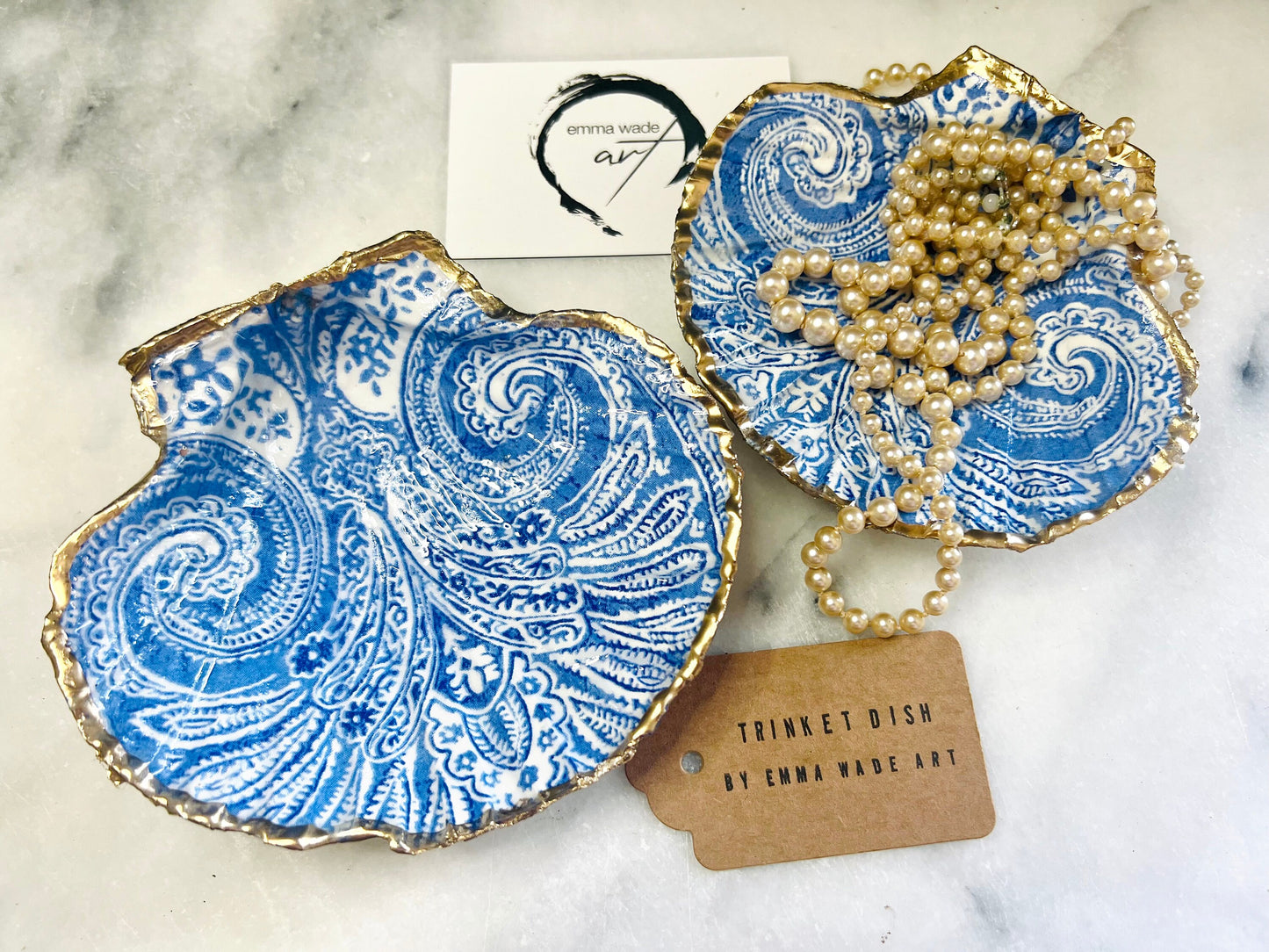Blue and white paisley scallop shell ring catcher with hand applied gold leaf edging and glossy resin finish. Handmade Dorset shell jewellery tray styled with pearls on a marble background. Coastal vanity decor and luxury beach house accessory gift.