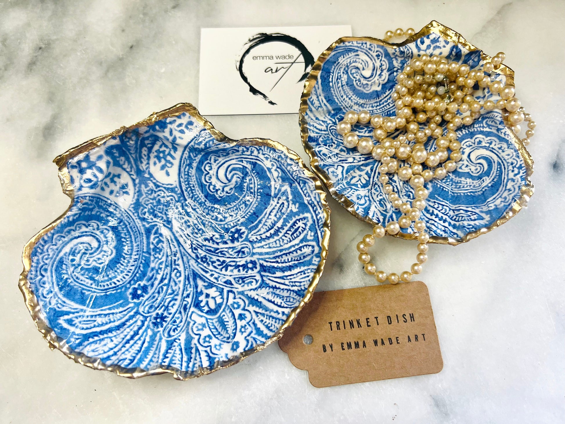 Blue and white paisley scallop shell ring catcher with hand applied gold leaf edging and glossy resin finish. Handmade Dorset shell jewellery tray styled with pearls on a marble background. Coastal vanity decor and luxury beach house accessory gift.