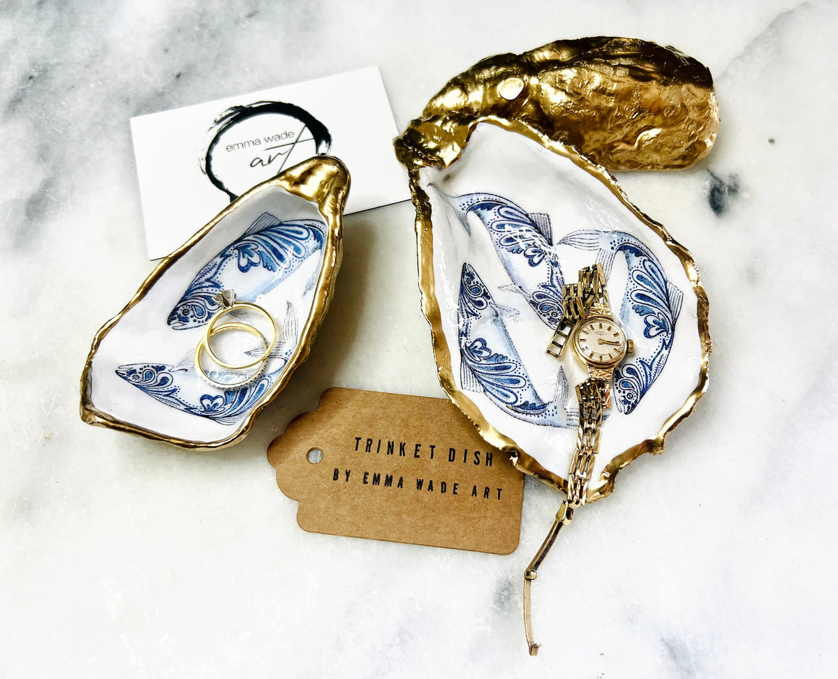 Handmade Dorset oyster shell trinket dish with blue and white paisley fish design, gold leaf gilded edges and glossy resin finish. Coastal jewellery holder and ring dish, photographed on a light surface showing the natural shell shape and pearly interior. Unique sustainably sourced shell, sold individually as a decorative coastal home décor accent or gift.