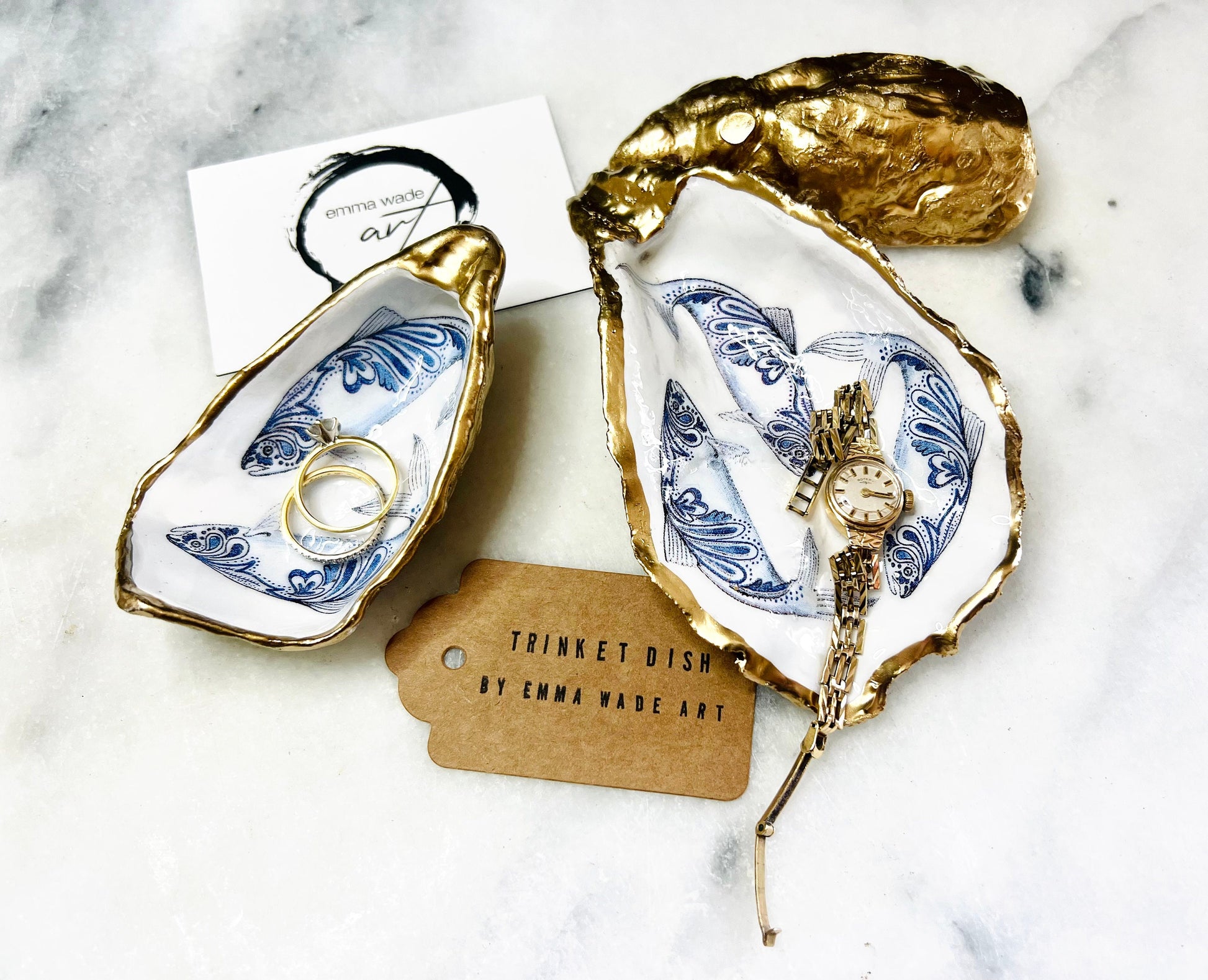 Handmade Dorset oyster shell trinket dish with blue and white paisley fish design, gold leaf gilded edges and glossy resin finish. Coastal jewellery holder and ring dish, photographed on a light surface showing the natural shell shape and pearly interior. Unique sustainably sourced shell, sold individually as a decorative coastal home décor accent or gift.