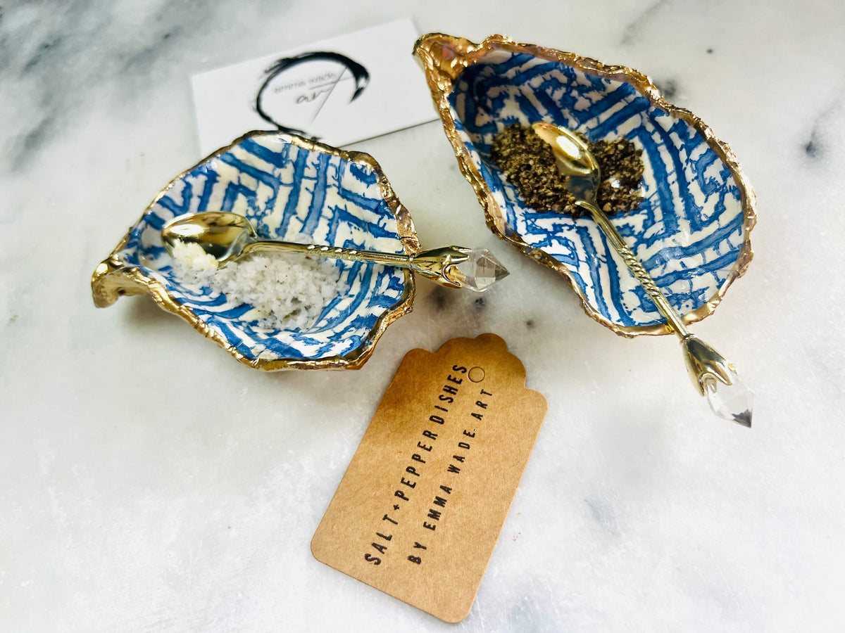 Handmade blue fretwork oyster shell salt and pepper pinch pots shown as a matching pair with small gold spoons, crafted from natural Dorset oyster shells. Each shell features a striking blue fretwork maze pattern, sealed with crystal-clear food-safe resin and finished with shimmering gold leaf edges. Coastal-inspired shell cruet dishes, perfect for table decor, weddings, or a unique luxury hostess gift, with each piece one of a kind.