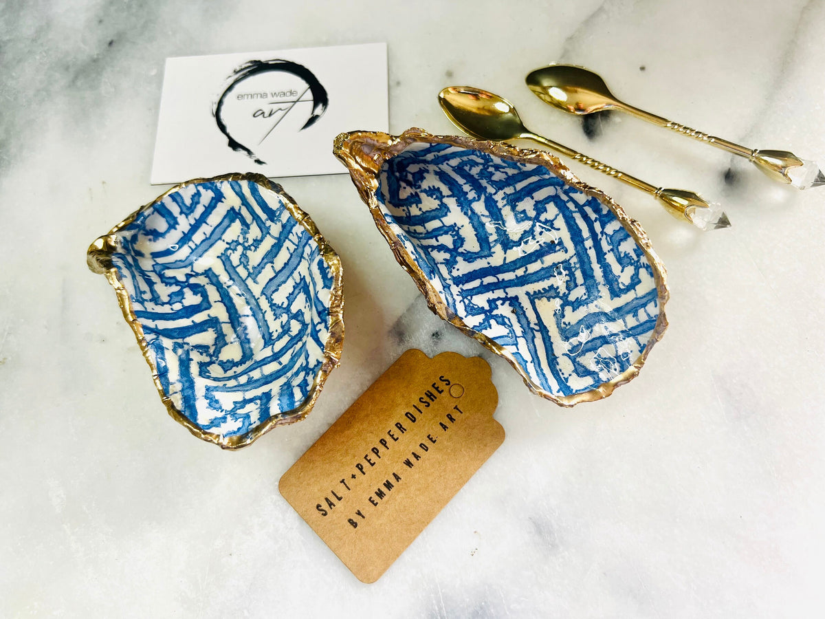 Handmade blue fretwork oyster shell salt and pepper pinch pots shown as a matching pair with small gold spoons, crafted from natural Dorset oyster shells. Each shell features a striking blue fretwork maze pattern, sealed with crystal-clear food-safe resin and finished with shimmering gold leaf edges. Coastal-inspired shell cruet dishes, perfect for table decor, weddings, or a unique luxury hostess gift, with each piece one of a kind.