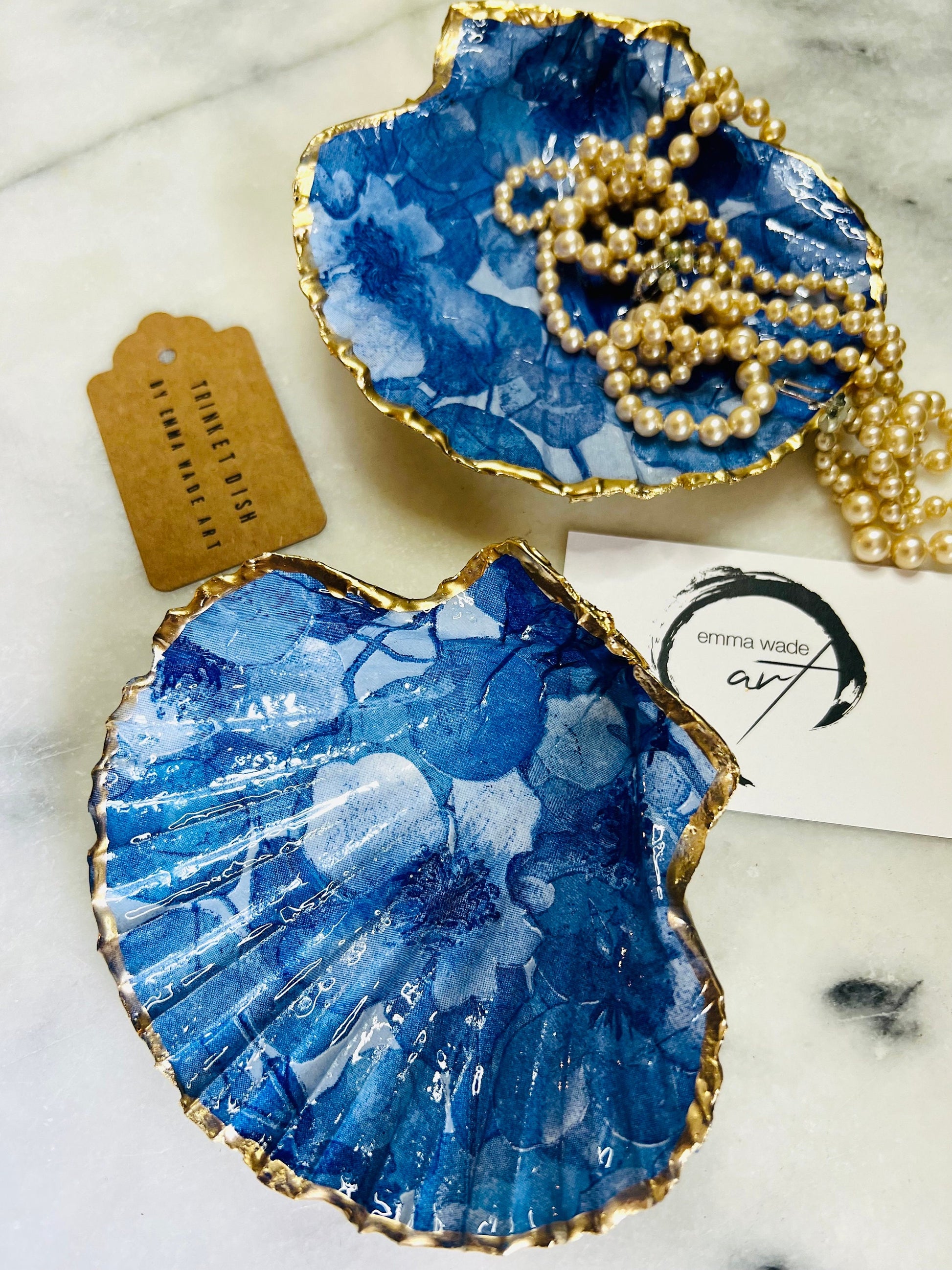 Deep blue watercolour floral scallop shell trinket dish with hand gilded gold leaf edging and glossy resin finish. Handmade Dorset shell jewellery holder in rich cobalt and ocean blue tones, styled as coastal home décor with pearls and gold details.