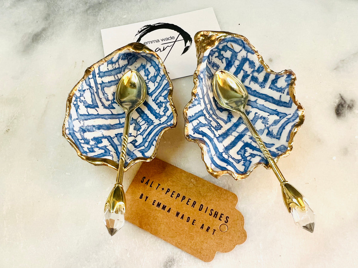 Handmade blue fretwork oyster shell salt and pepper pinch pots shown as a matching pair with small gold spoons, crafted from natural Dorset oyster shells. Each shell features a striking blue fretwork maze pattern, sealed with crystal-clear food-safe resin and finished with shimmering gold leaf edges. Coastal-inspired shell cruet dishes, perfect for table decor, weddings, or a unique luxury hostess gift, with each piece one of a kind.