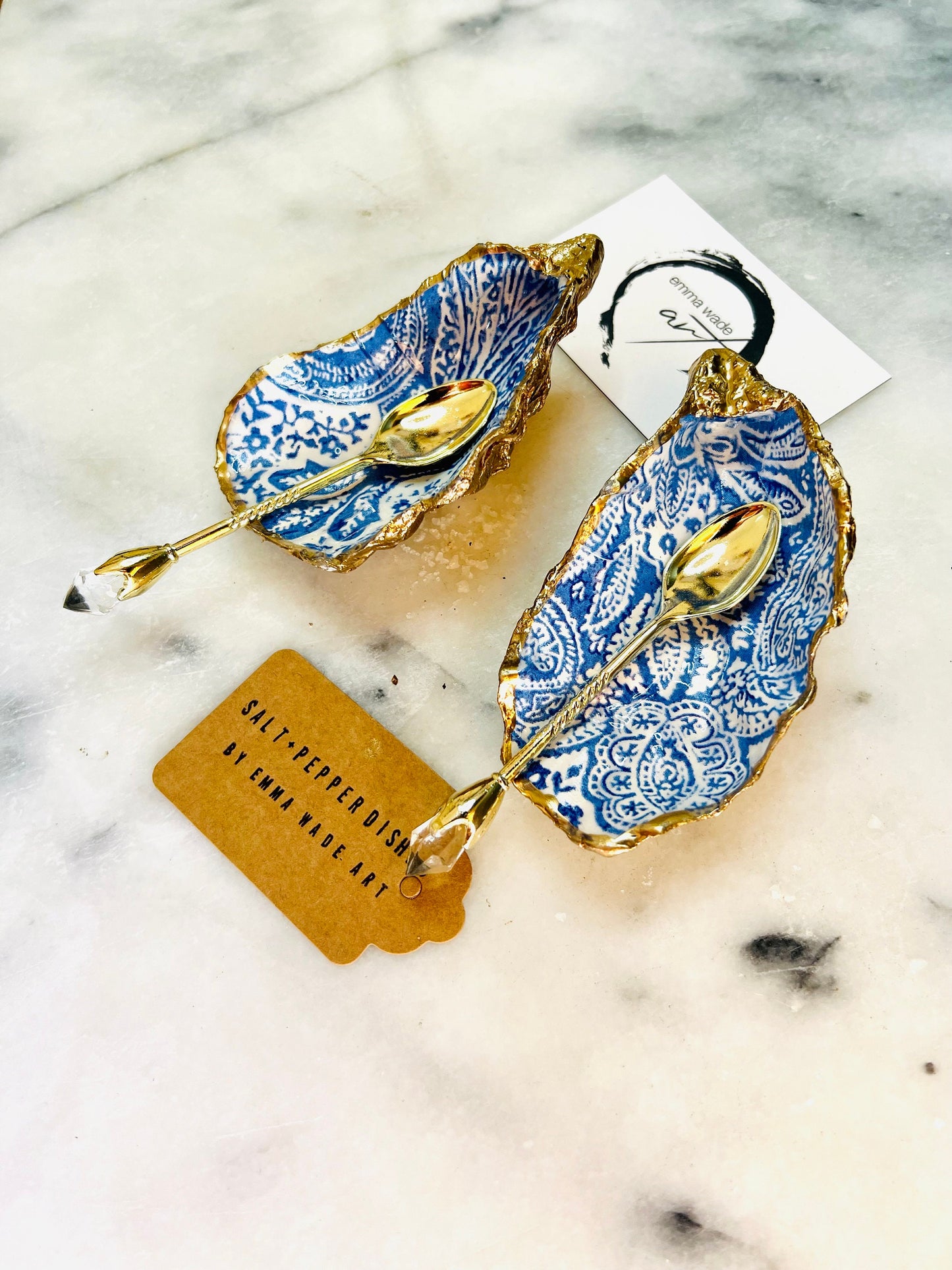 Pair of blue and white paisley oyster shell salt cellar set with gold leaf edging and matching gold crystal spoons. Handmade Dorset oyster shell pinch pots finished in glossy food safe resin. Coastal dining decor and luxury beach house table accessory.
