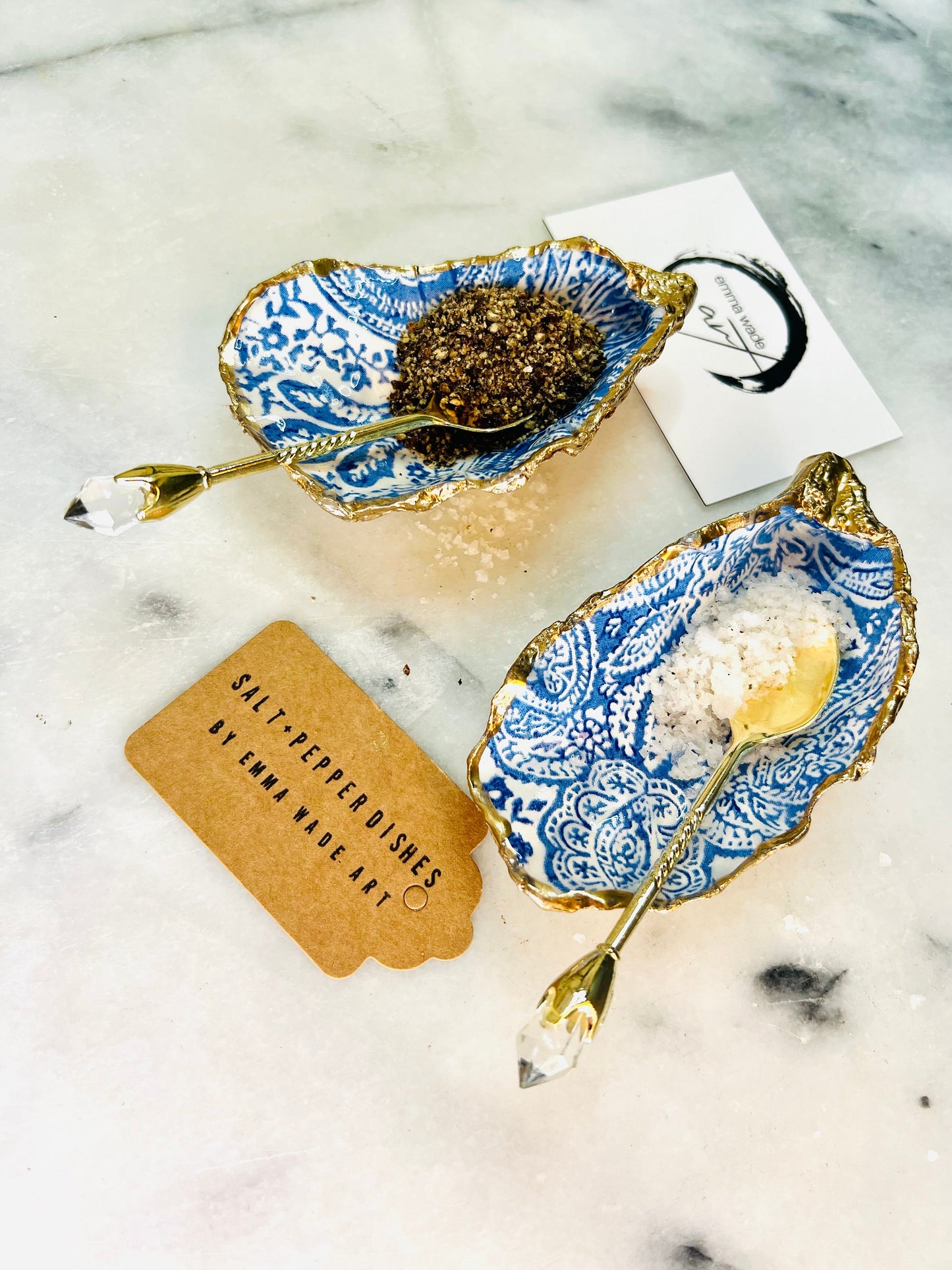 Blue and white paisley oyster shell salt cellar set with gold leaf edging and matching gold crystal spoons. Handmade Dorset oyster shell pinch pots finished in glossy food safe resin. Coastal dining decor and luxury beach house table accessory.