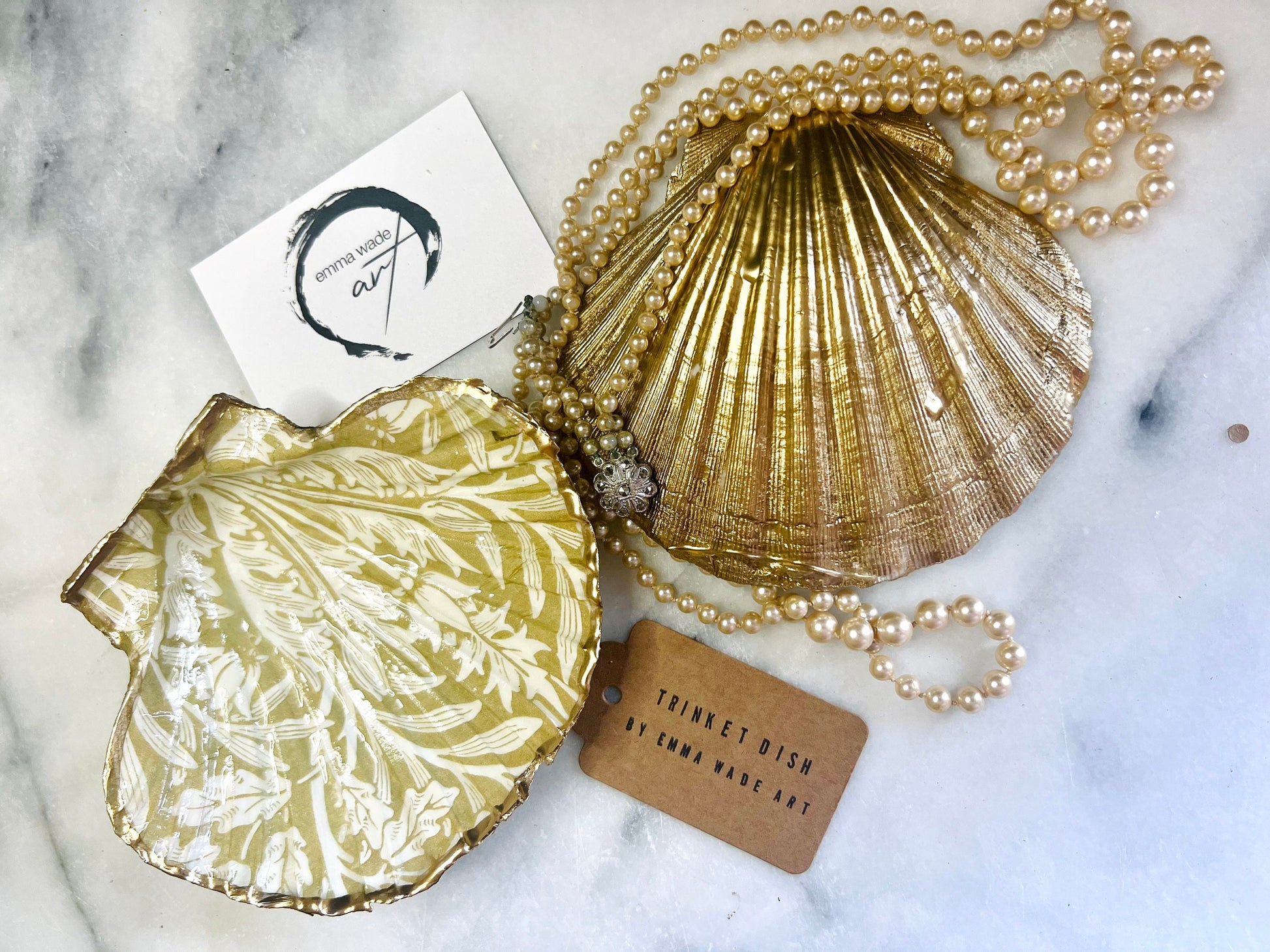 Handmade scallop shell trinket dishes featuring a William Morris gold and ivory acorn heritage pattern with shimmering liquid gold leaf edging. Natural Dorset scallop shells sealed in glossy crystal clear resin and styled as luxury jewellery holders, vanity trays and coastal home décor accessories. Elegant Arts and Crafts inspired shell dishes photographed on a marble background with pearls and decorative styling.