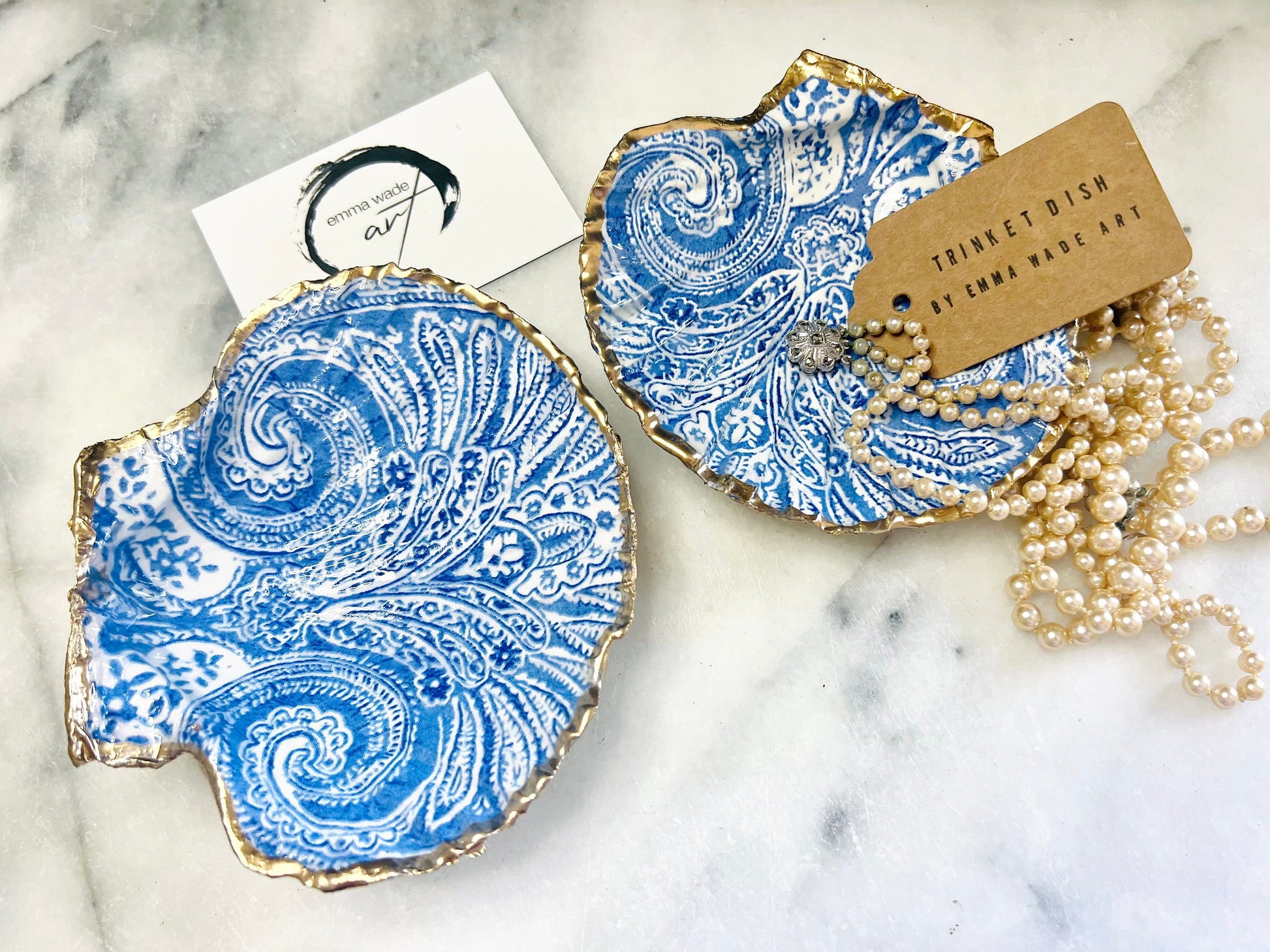 Blue and white paisley scallop shell ring catcher with hand applied gold leaf edging and glossy resin finish. Handmade Dorset shell jewellery tray styled with pearls on a marble background. Coastal vanity decor and luxury beach house accessory gift.