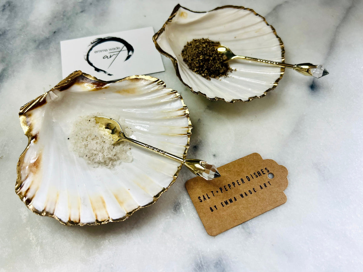 Pair of handmade Dorset scallop shell salt and pepper pinch pots with polished pearl finish, gold leaf edging, and optional gold crystal spoons or serving tongs. Elegant coastal shell cruet set styled for luxury dining and wedding table décor.