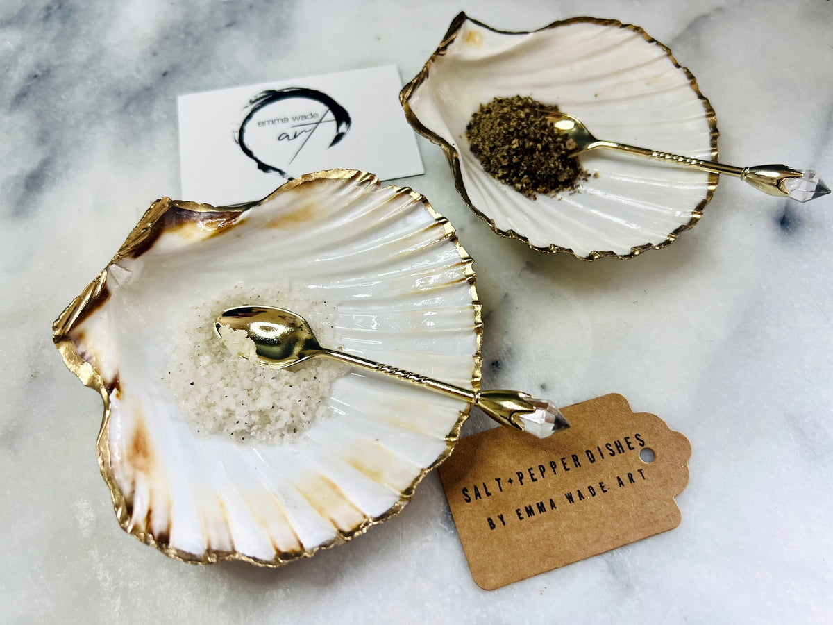 Pair of handmade Dorset scallop shell salt and pepper pinch pots with polished pearl finish, gold leaf edging, and optional gold crystal spoons or serving tongs. Elegant coastal shell cruet set styled for luxury dining and wedding table décor.