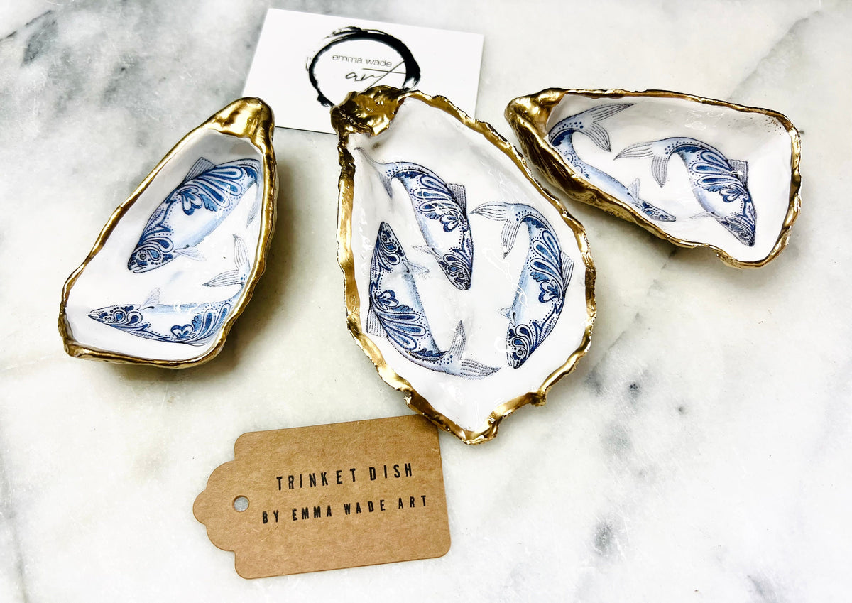 Handmade Dorset oyster shell trinket dish with blue and white paisley fish design, gold leaf gilded edges and glossy resin finish. Coastal jewellery holder and ring dish, photographed on a light surface showing the natural shell shape and pearly interior. Unique sustainably sourced shell, sold individually as a decorative coastal home décor accent or gift.
