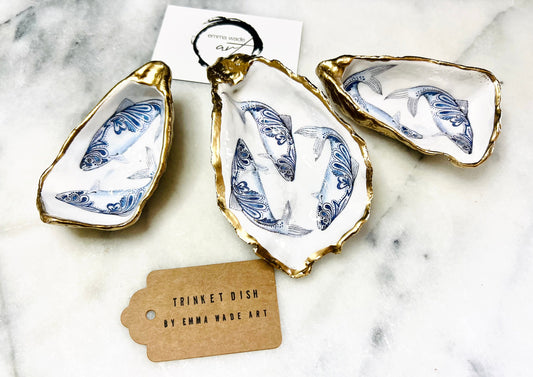 Handmade Dorset oyster shell trinket dish with blue and white paisley fish design, gold leaf gilded edges and glossy resin finish. Coastal jewellery holder and ring dish, photographed on a light surface showing the natural shell shape and pearly interior. Unique sustainably sourced shell, sold individually as a decorative coastal home décor accent or gift.