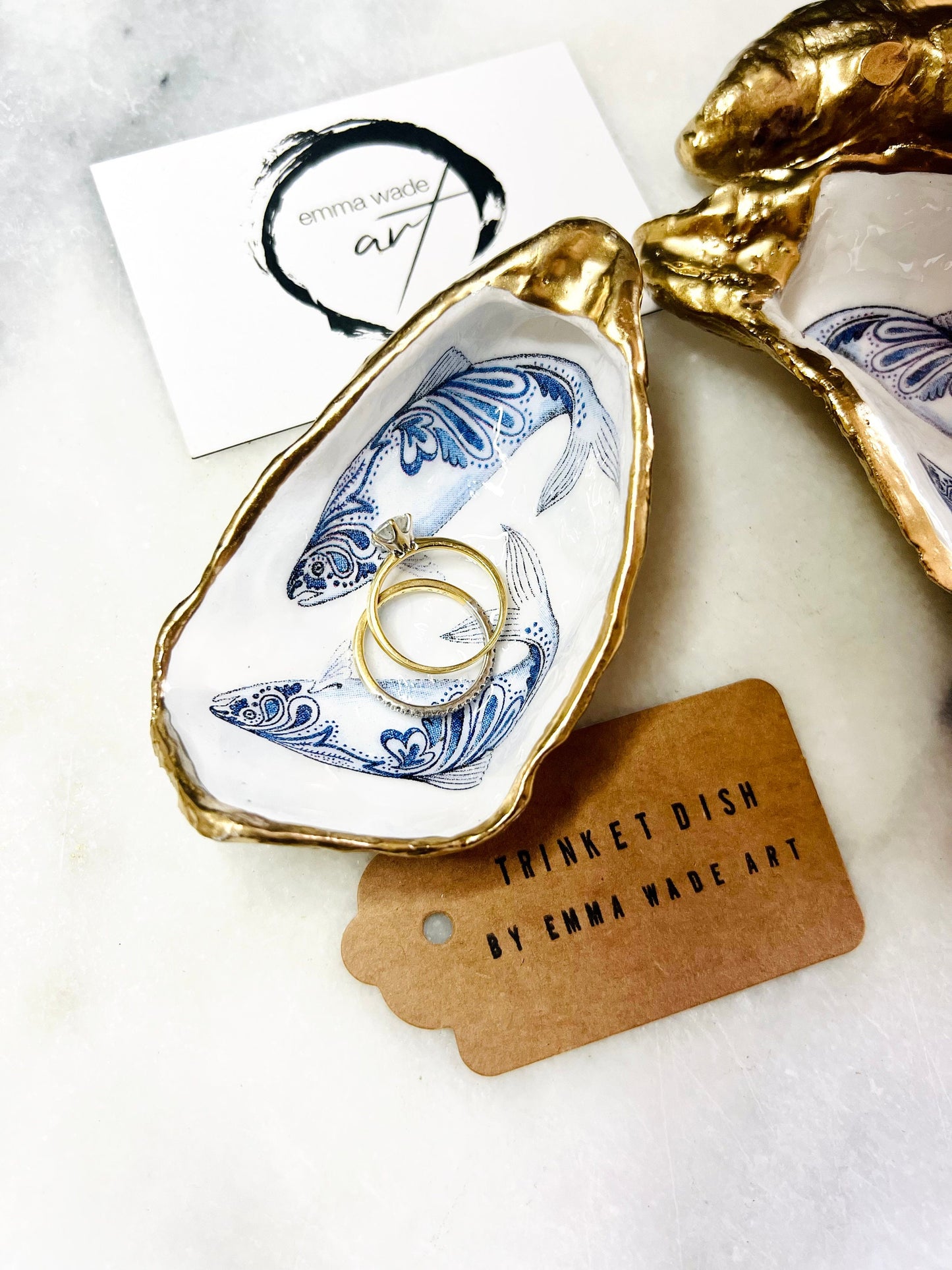 Handmade Dorset oyster shell trinket dish with blue and white paisley fish design, gold leaf gilded edges and glossy resin finish. Coastal jewellery holder and ring dish, photographed on a light surface showing the natural shell shape and pearly interior. Unique sustainably sourced shell, sold individually as a decorative coastal home décor accent or gift.