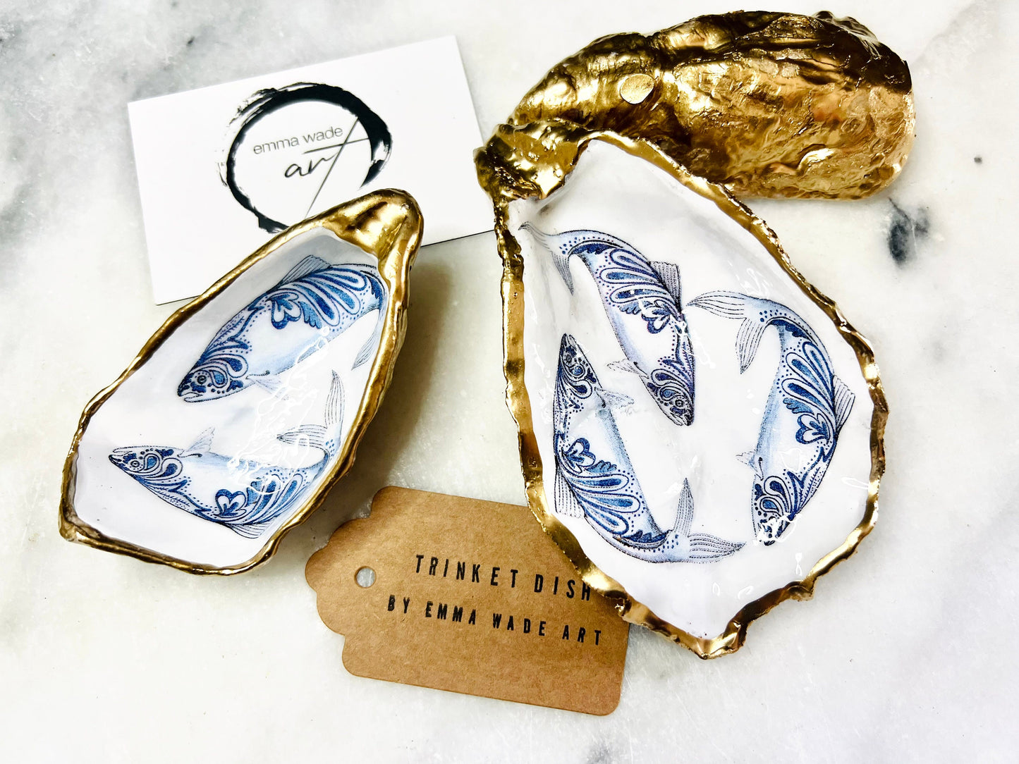 Handmade Dorset oyster shell trinket dish with blue and white paisley fish design, gold leaf gilded edges and glossy resin finish. Coastal jewellery holder and ring dish, photographed on a light surface showing the natural shell shape and pearly interior. Unique sustainably sourced shell, sold individually as a decorative coastal home décor accent or gift.