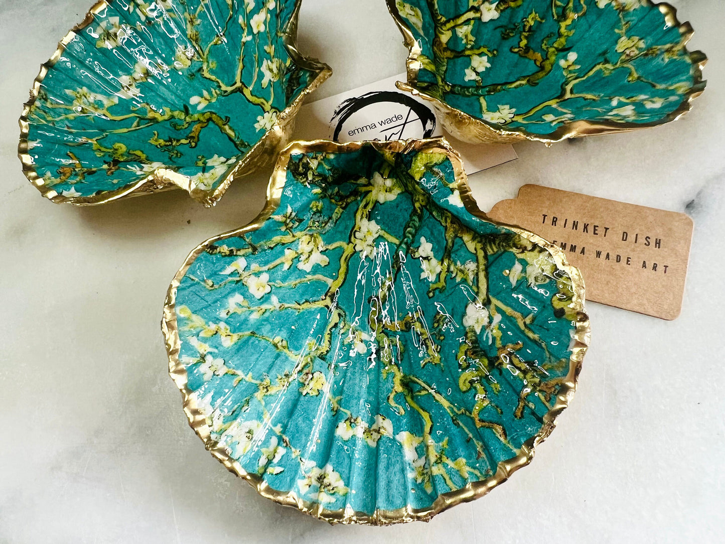Handcrafted Dorset scallop shell trinket dish inspired by Vincent van Gogh’s Almond Blossom painting. Turquoise blue and green background with branching blossom design and raised gold detailing, finished with liquid gold leaf edging and sealed in high-gloss resin. Decorative shell jewellery holder styled on marble surface, suitable for rings, earrings, trinkets or as a tea light holder. Coastal art-inspired home decor piece.