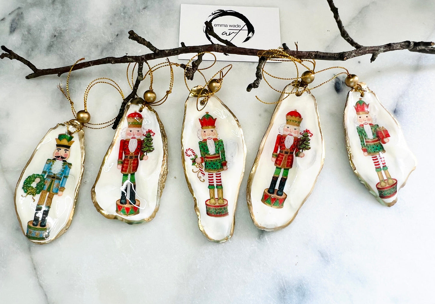 Handmade Nutcracker oyster shell Christmas ornaments with gold gilded edges and glossy resin finish. Traditional festive Nutcracker designs on natural pearl Dorset oyster shells in red, green, aqua, blue and gold tones, styled as luxury coastal Christmas tree decorations.