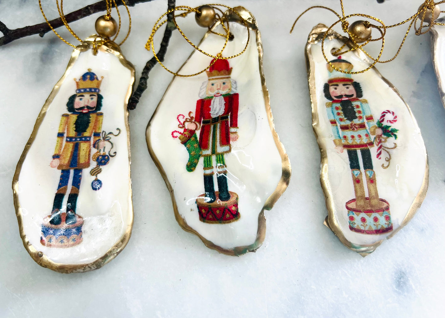 Handmade Nutcracker oyster shell Christmas ornaments with gold gilded edges and glossy resin finish. Traditional festive Nutcracker designs on natural pearl Dorset oyster shells in red, green, aqua, blue and gold tones, styled as luxury coastal Christmas tree decorations.