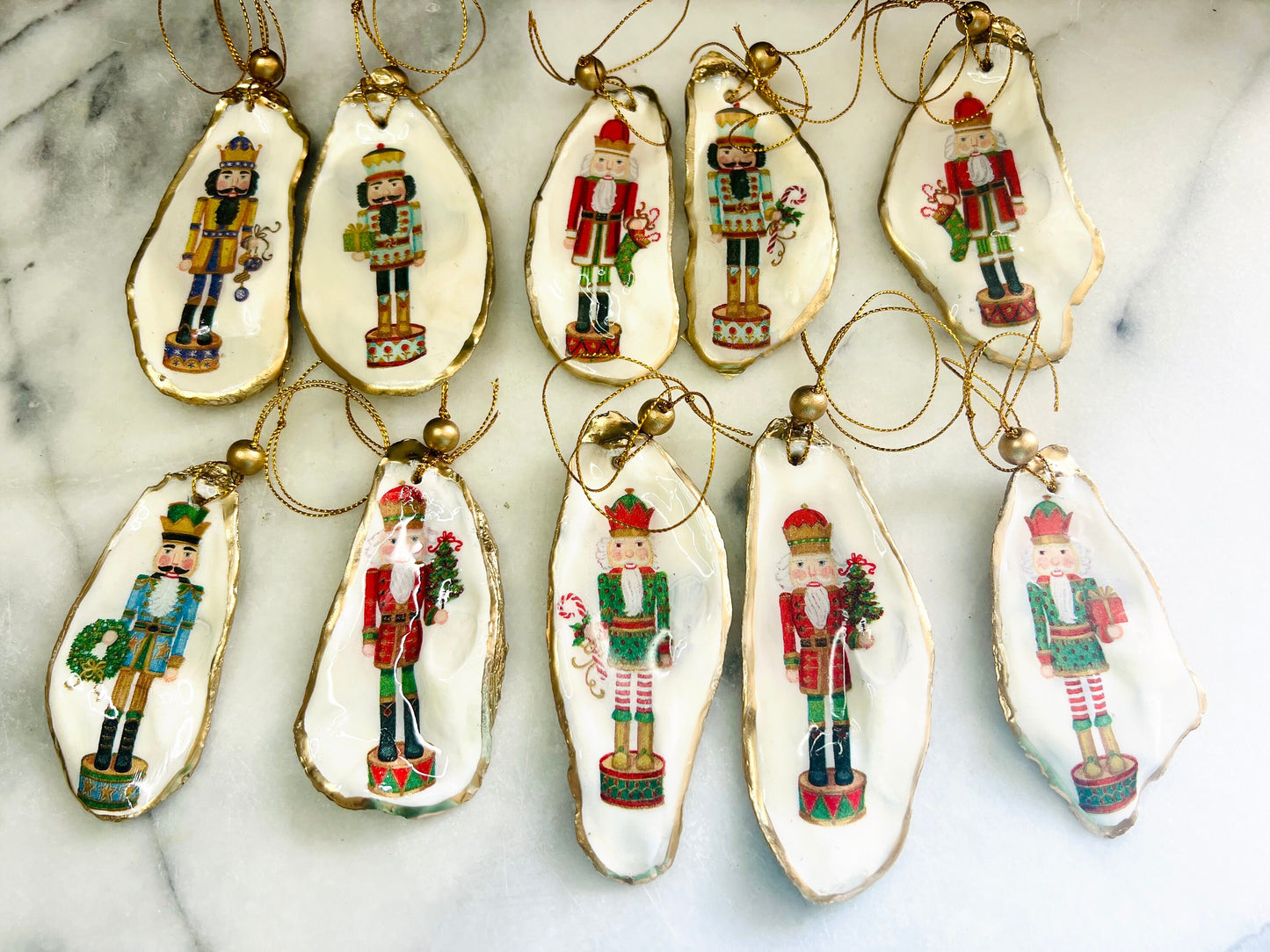 Handmade Nutcracker oyster shell Christmas ornaments with gold gilded edges and glossy resin finish. Traditional festive Nutcracker designs on natural pearl Dorset oyster shells in red, green, aqua, blue and gold tones, styled as luxury coastal Christmas tree decorations.
