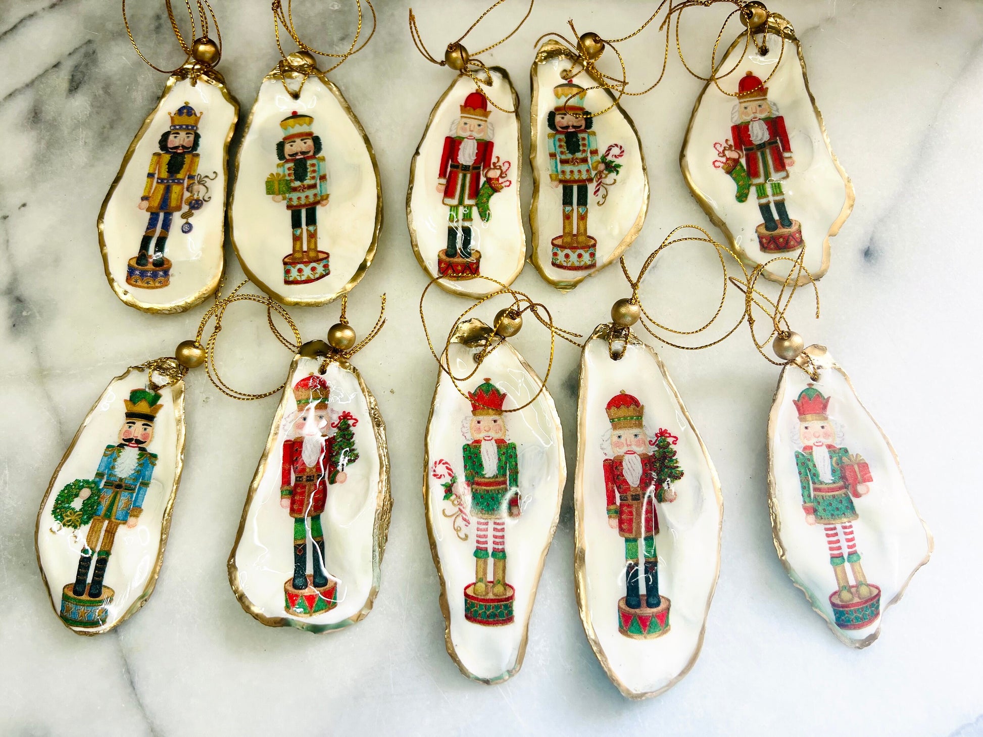 Handmade Nutcracker oyster shell Christmas ornaments with gold gilded edges and glossy resin finish. Traditional festive Nutcracker designs on natural pearl Dorset oyster shells in red, green, aqua, blue and gold tones, styled as luxury coastal Christmas tree decorations.