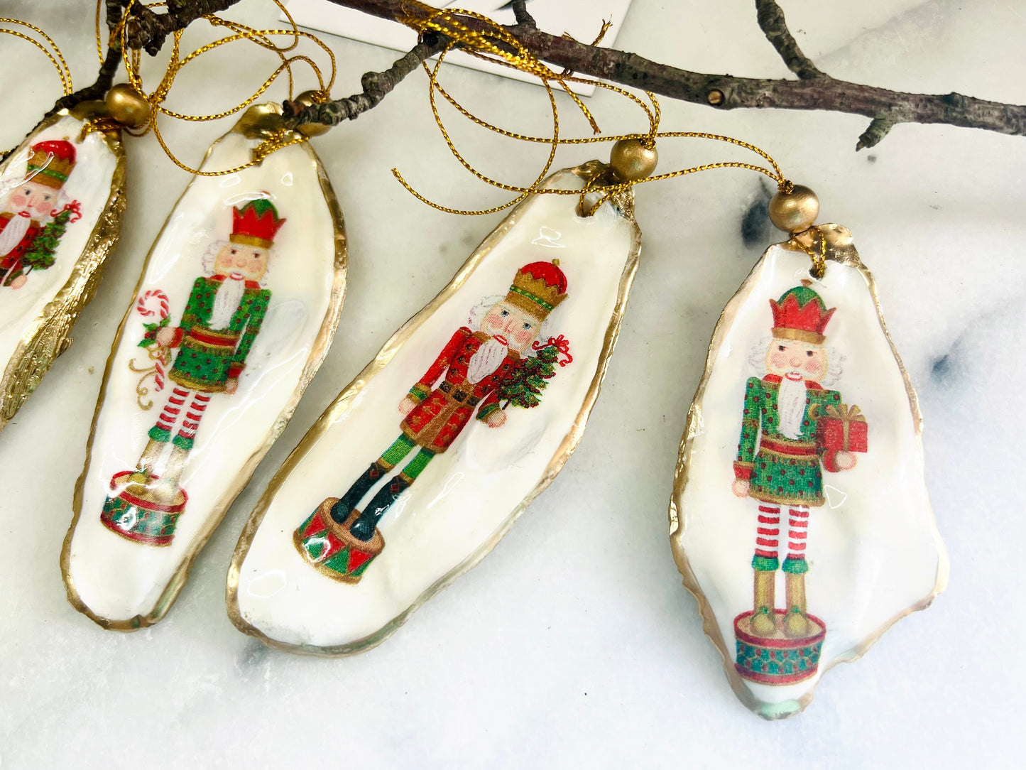 Handmade Nutcracker oyster shell Christmas ornaments with gold gilded edges and glossy resin finish. Traditional festive Nutcracker designs on natural pearl Dorset oyster shells in red, green, aqua, blue and gold tones, styled as luxury coastal Christmas tree decorations.