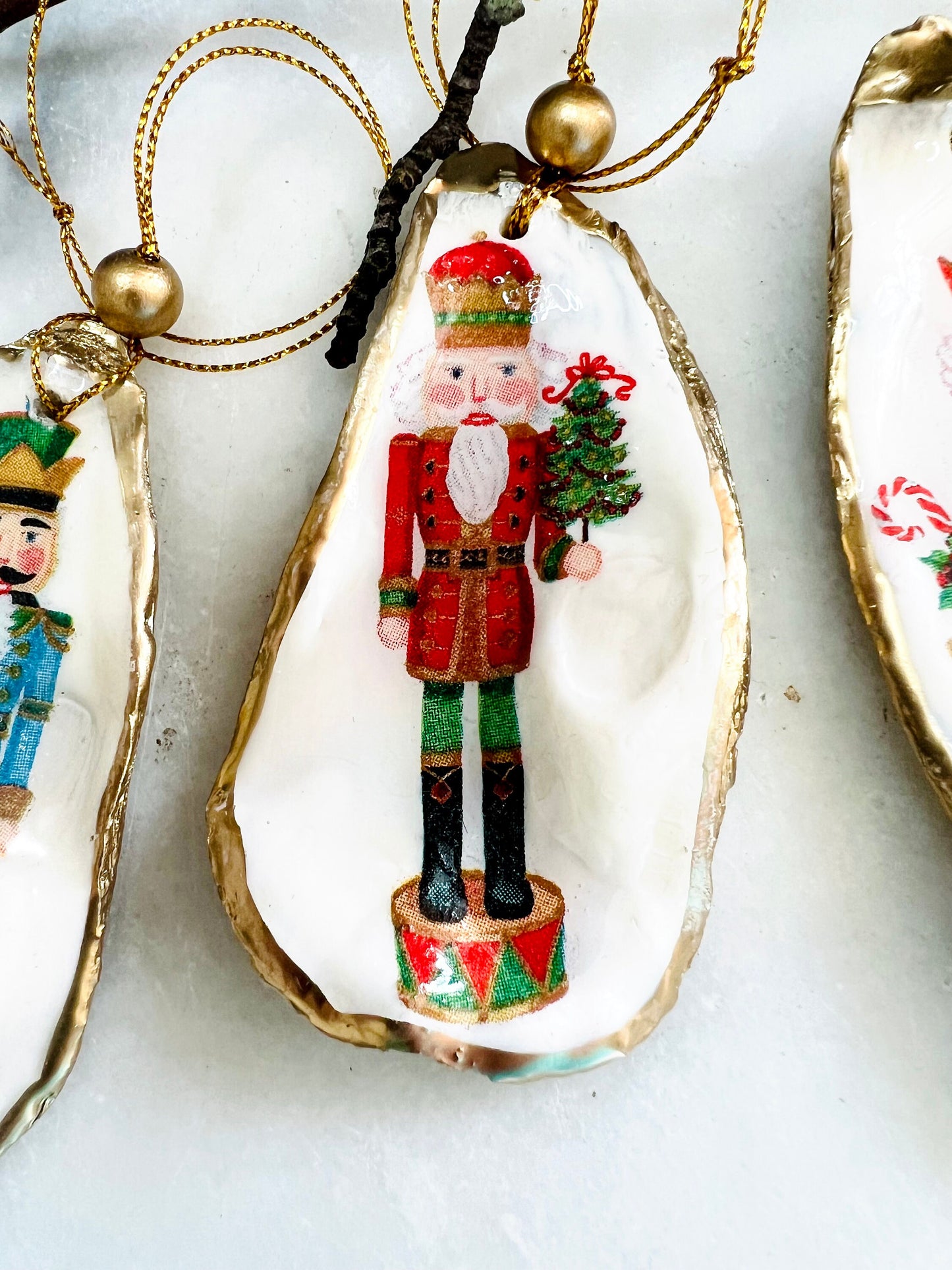 Handmade Nutcracker oyster shell Christmas ornaments with gold gilded edges and glossy resin finish. Traditional festive Nutcracker designs on natural pearl Dorset oyster shells in red, green, aqua, blue and gold tones, styled as luxury coastal Christmas tree decorations.