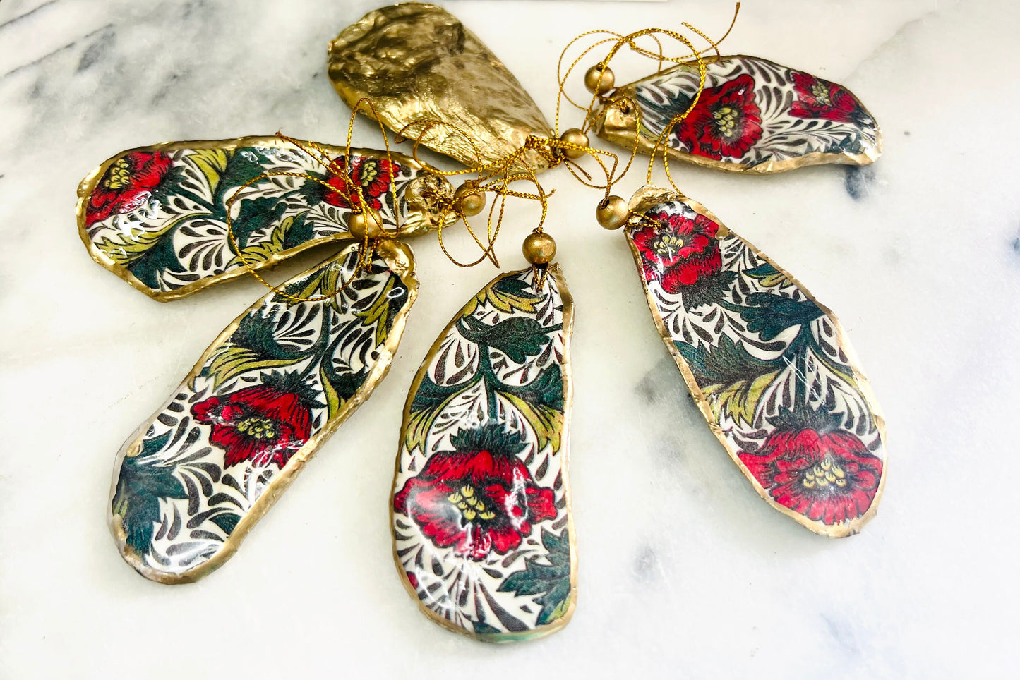 Handmade Dorset oyster shell hanging ornaments featuring William Morris inspired Red Peony botanical floral design in rich red, cream and deep green tones. Natural oyster shells with polished pearlescent interiors, hand edged with liquid gold leaf and sealed with glossy resin for shine and durability. Elegant botanical coastal décor suitable as Christmas ornaments, floral hanging décor, cottagecore home accessories or thoughtful artisan gifts. Available individually or as curated sets.