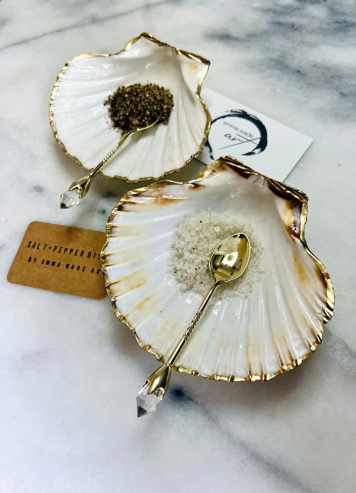Pair of handmade Dorset scallop shell salt and pepper pinch pots with polished pearl finish, gold leaf edging, and optional gold crystal spoons or serving tongs. Elegant coastal shell cruet set styled for luxury dining and wedding table décor.