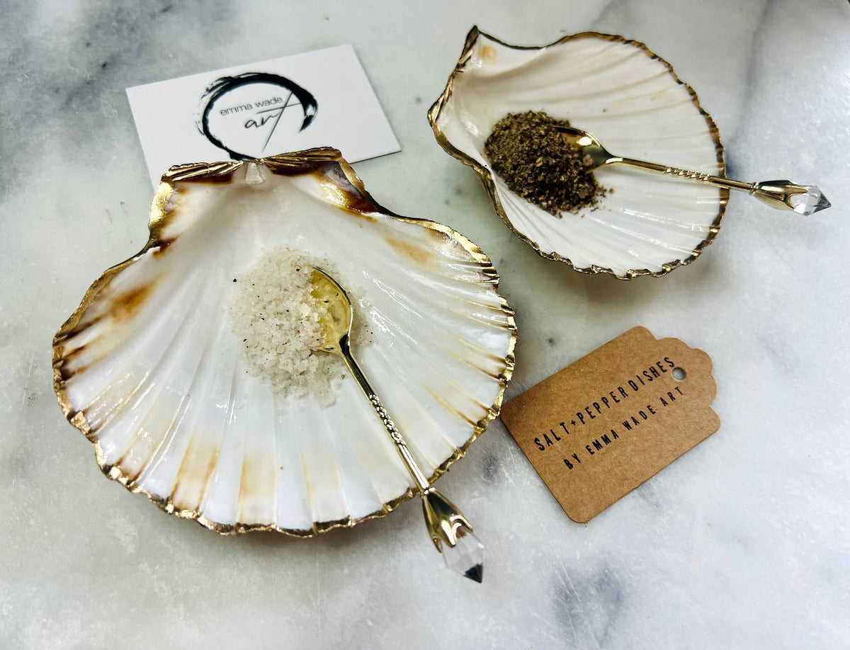 Pair of handmade Dorset scallop shell salt and pepper pinch pots with polished pearl finish, gold leaf edging, and optional gold crystal spoons or serving tongs. Elegant coastal shell cruet set styled for luxury dining and wedding table décor.