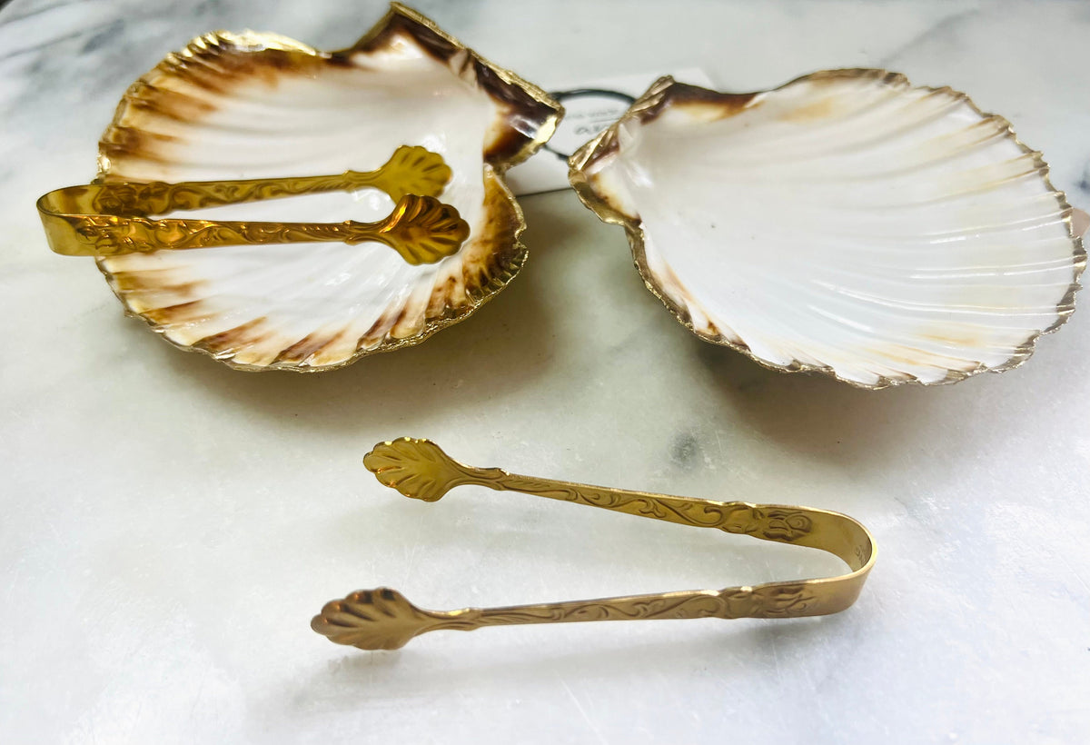 Pair of handmade Dorset scallop shell salt and pepper pinch pots with polished pearl finish, gold leaf edging, and optional gold crystal spoons or serving tongs. Elegant coastal shell cruet set styled for luxury dining and wedding table décor.