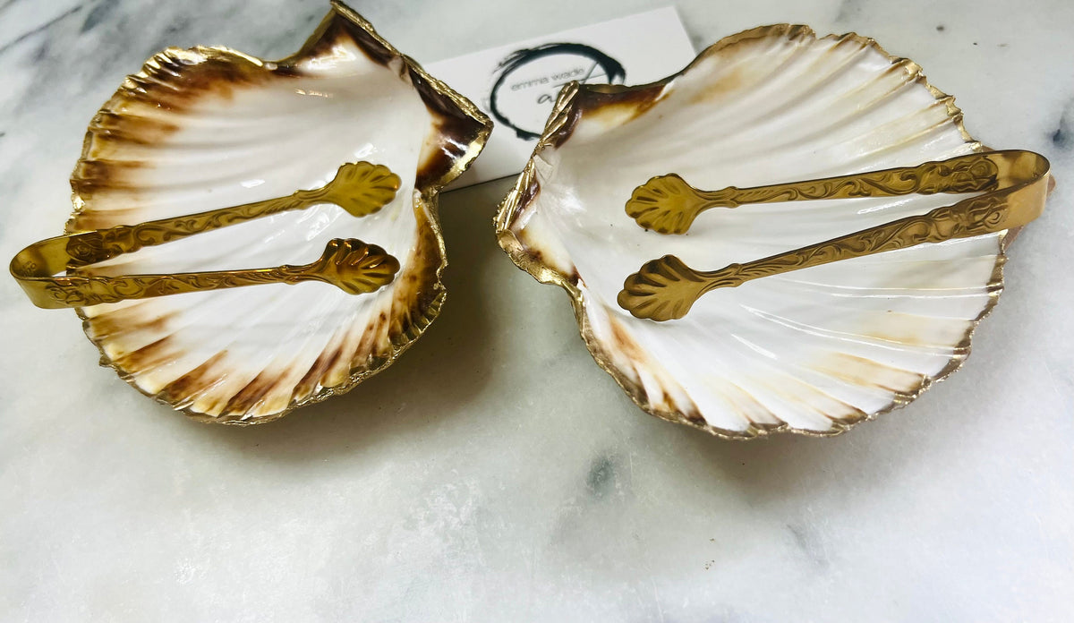 Pair of handmade Dorset scallop shell salt and pepper pinch pots with polished pearl finish, gold leaf edging, and optional gold crystal spoons or serving tongs. Elegant coastal shell cruet set styled for luxury dining and wedding table décor.