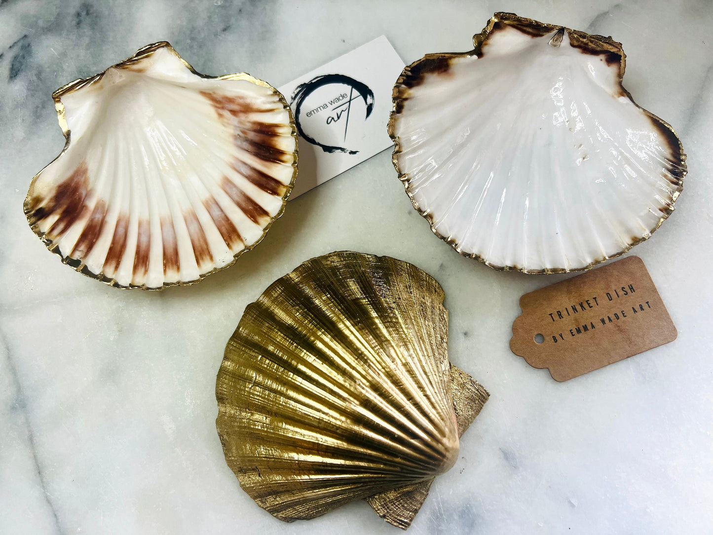 Handmade Dorset scallop shell trinket dishes featuring natural white shells with delicate liquid gold leaf speckling, hand-painted gold leaf edging and glossy crystal clear resin. Luxury coastal jewellery dishes styled on a white marble background with elegant neutral tones and artisan coastal home décor styling.