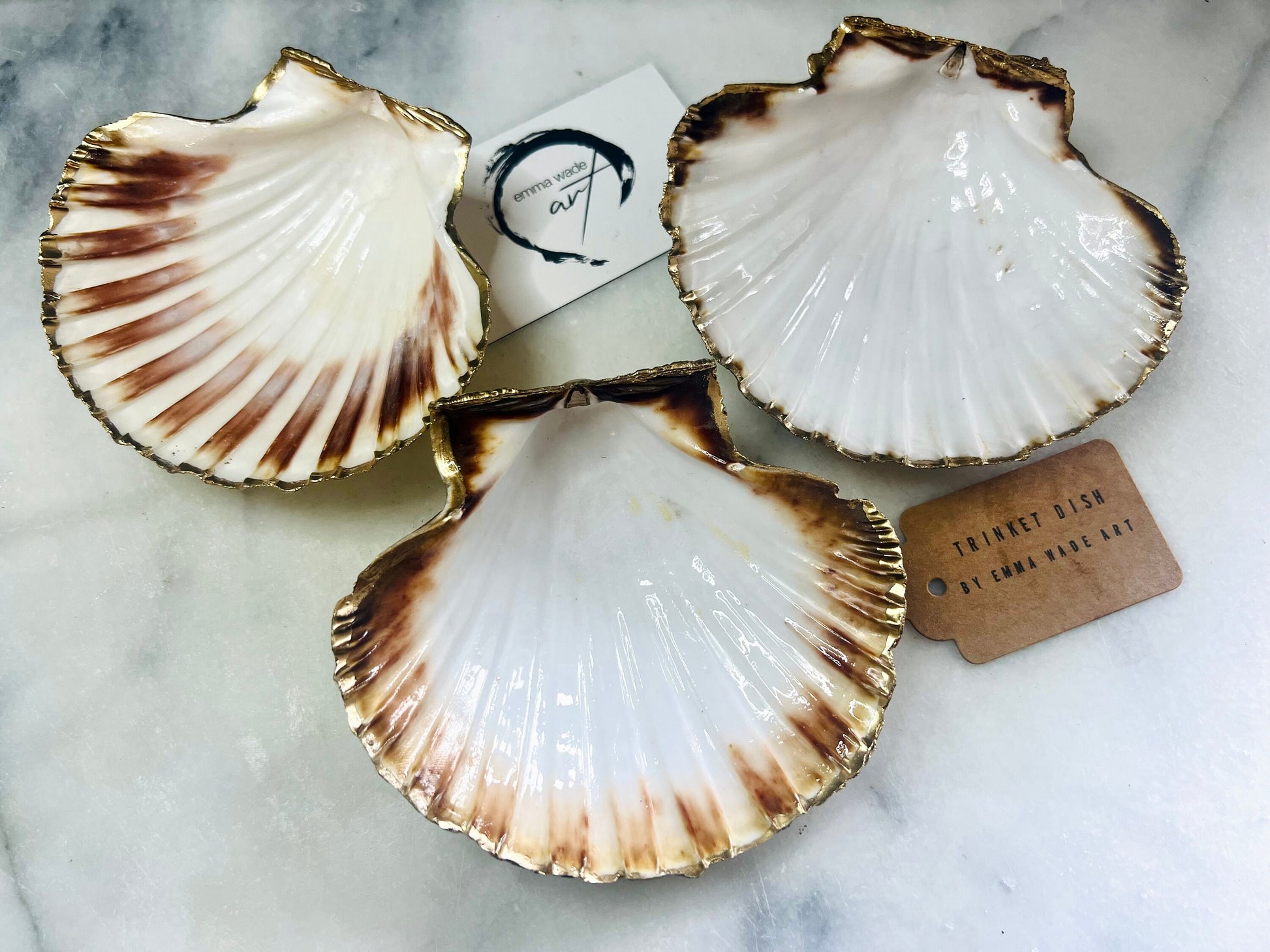 Handmade Dorset scallop shell trinket dishes featuring natural white shells with delicate liquid gold leaf speckling, hand-painted gold leaf edging and glossy crystal clear resin. Luxury coastal jewellery dishes styled on a white marble background with elegant neutral tones and artisan coastal home décor styling.
