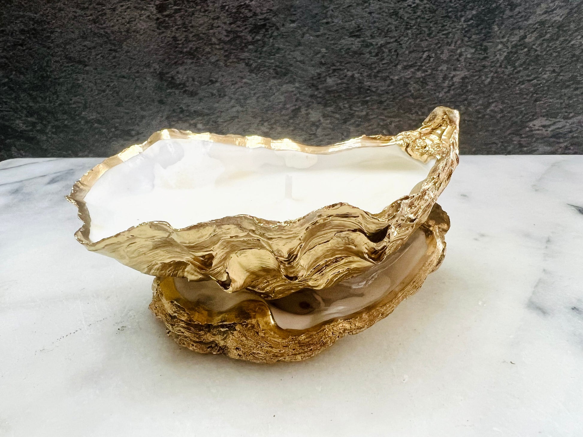 Luxury oyster shell candle hand poured with natural vegetable wax inside a real Dorset oyster shell with gold leaf edging. Coastal candle decor with polished pearl shell interior and artisan handmade styling. Sustainable shell candle gift for weddings, birthdays, spa decor and coastal home interiors.