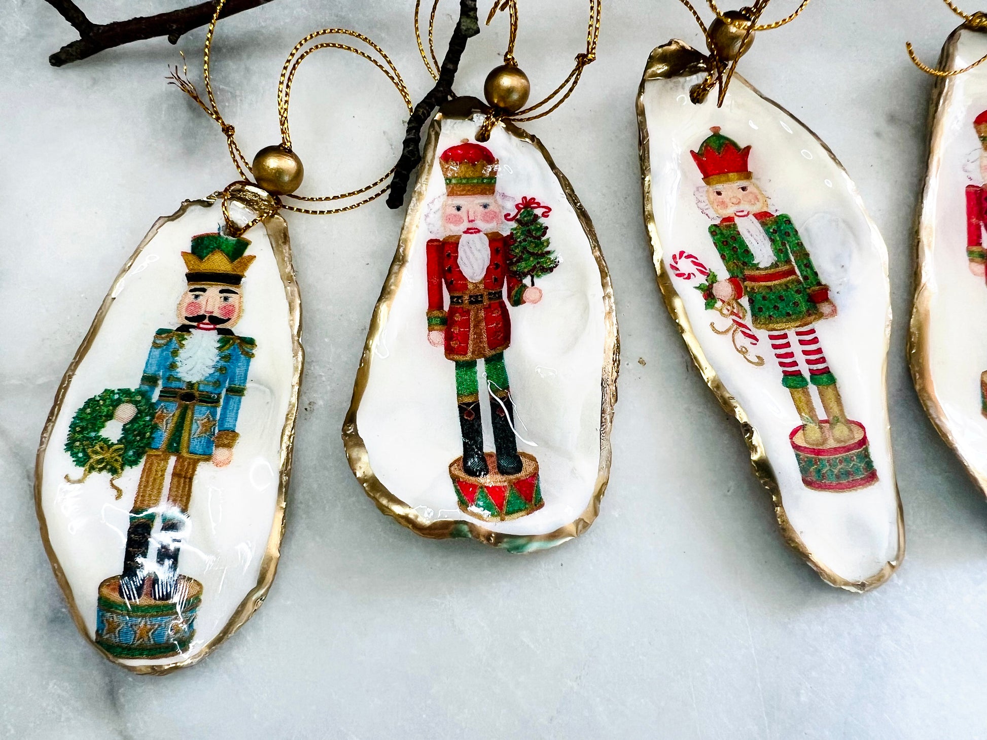 Handmade Nutcracker oyster shell Christmas ornaments with gold gilded edges and glossy resin finish. Traditional festive Nutcracker designs on natural pearl Dorset oyster shells in red, green, aqua, blue and gold tones, styled as luxury coastal Christmas tree decorations.