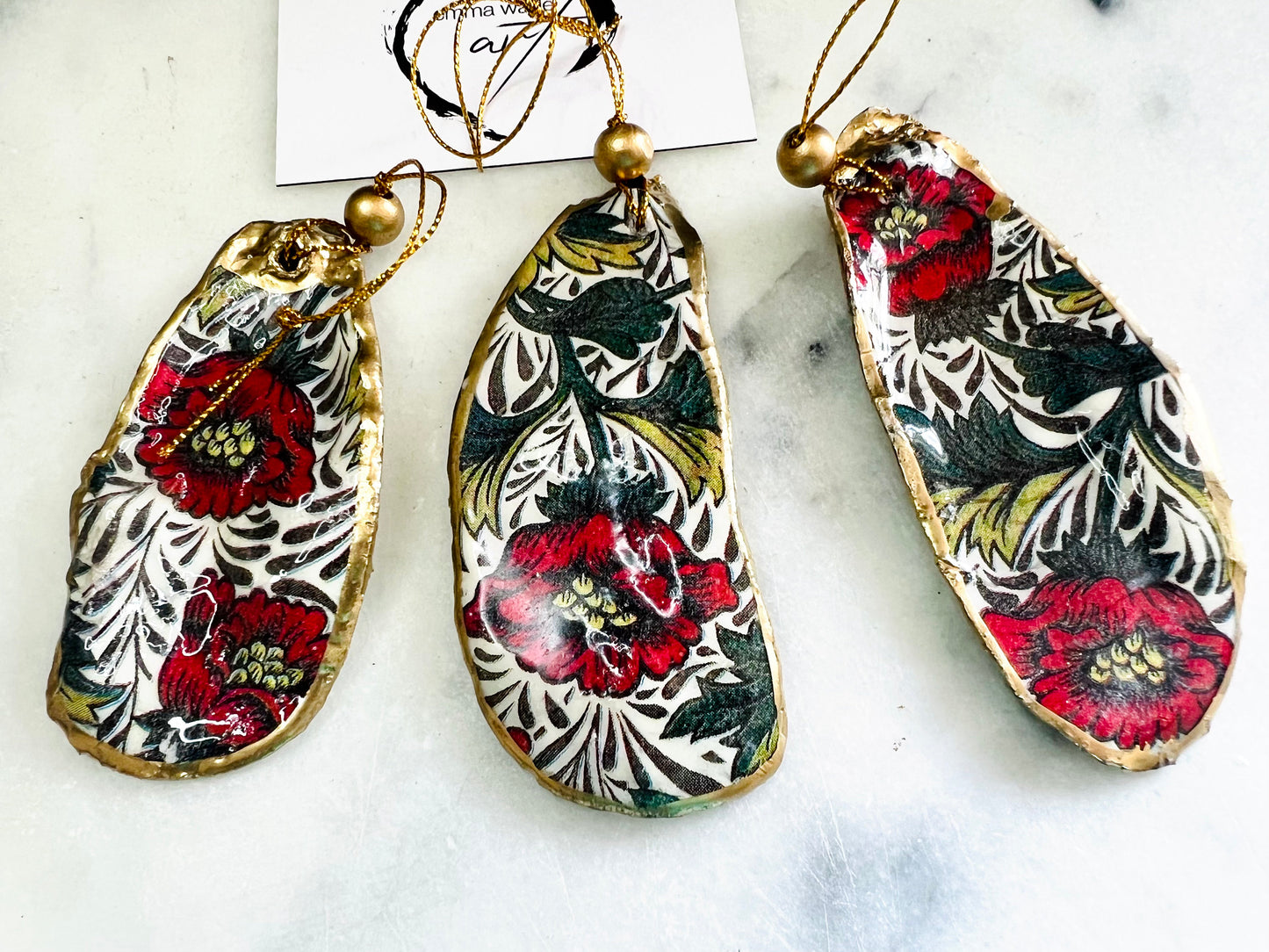 Handmade Dorset oyster shell hanging ornaments featuring William Morris inspired Red Peony botanical floral design in rich red, cream and deep green tones. Natural oyster shells with polished pearlescent interiors, hand edged with liquid gold leaf and sealed with glossy resin for shine and durability. Elegant botanical coastal décor suitable as Christmas ornaments, floral hanging décor, cottagecore home accessories or thoughtful artisan gifts. Available individually or as curated sets.