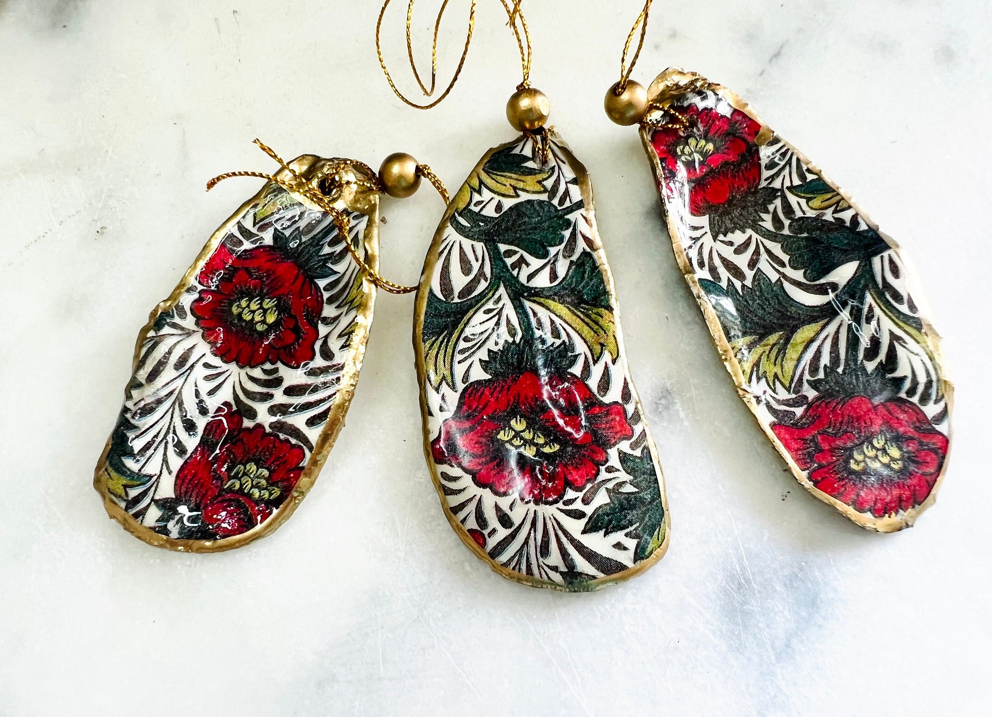 Handmade Dorset oyster shell hanging ornaments featuring William Morris inspired Red Peony botanical floral design in rich red, cream and deep green tones. Natural oyster shells with polished pearlescent interiors, hand edged with liquid gold leaf and sealed with glossy resin for shine and durability. Elegant botanical coastal décor suitable as Christmas ornaments, floral hanging décor, cottagecore home accessories or thoughtful artisan gifts. Available individually or as curated sets.