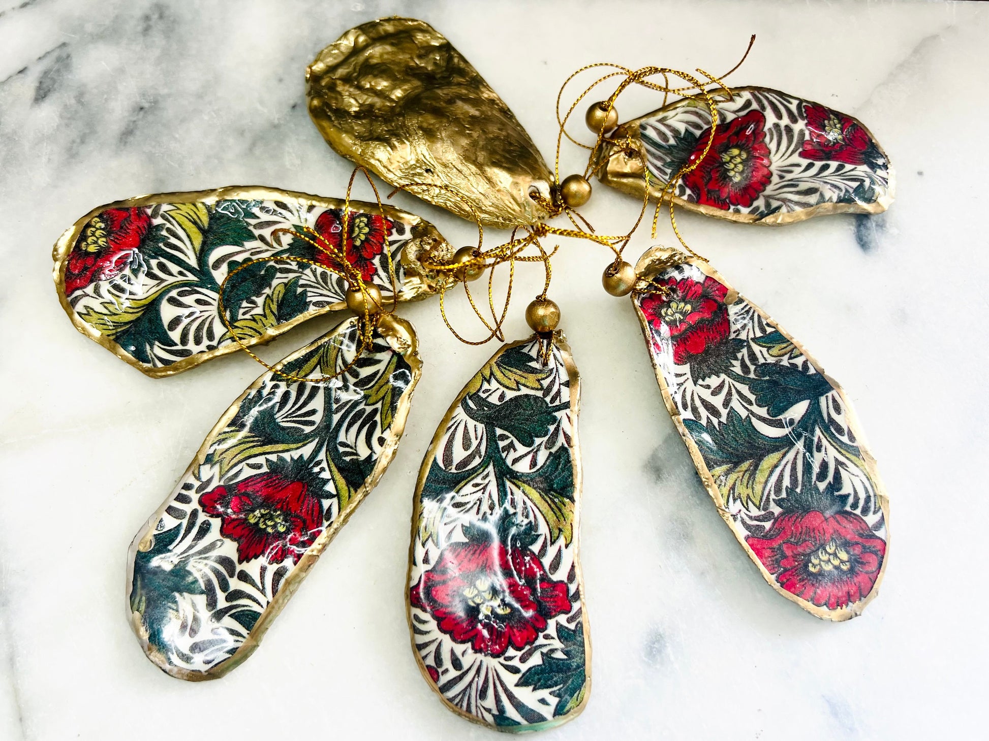 Handmade Dorset oyster shell hanging ornaments featuring William Morris inspired Red Peony botanical floral design in rich red, cream and deep green tones. Natural oyster shells with polished pearlescent interiors, hand edged with liquid gold leaf and sealed with glossy resin for shine and durability. Elegant botanical coastal décor suitable as Christmas ornaments, floral hanging décor, cottagecore home accessories or thoughtful artisan gifts. Available individually or as curated sets.