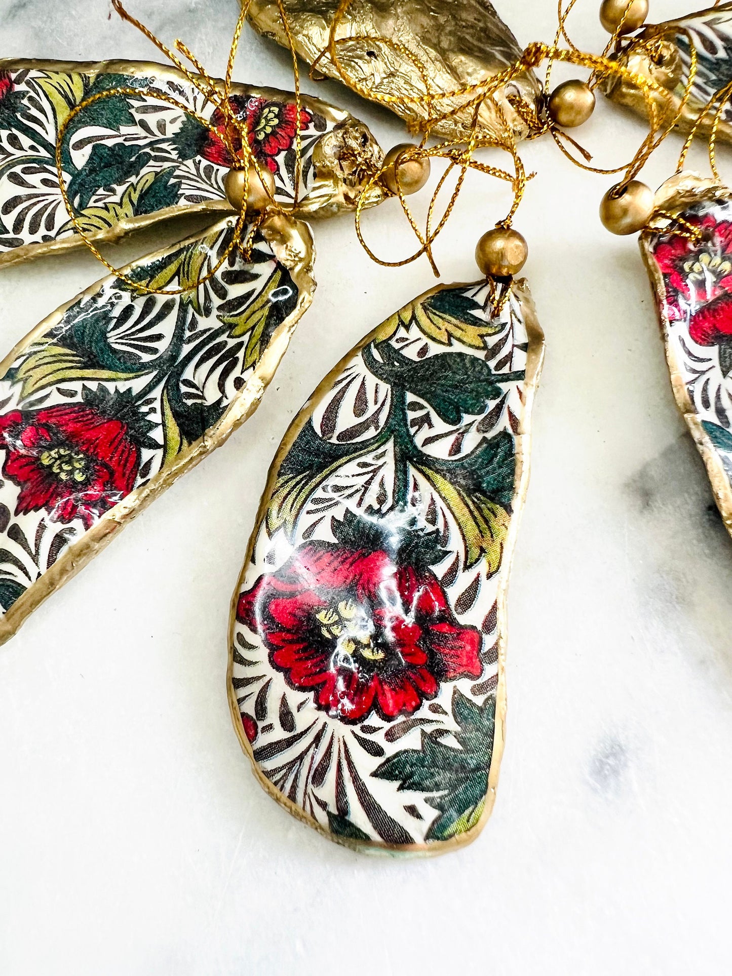Handmade Dorset oyster shell hanging ornaments featuring William Morris inspired Red Peony botanical floral design in rich red, cream and deep green tones. Natural oyster shells with polished pearlescent interiors, hand edged with liquid gold leaf and sealed with glossy resin for shine and durability. Elegant botanical coastal décor suitable as Christmas ornaments, floral hanging décor, cottagecore home accessories or thoughtful artisan gifts. Available individually or as curated sets.