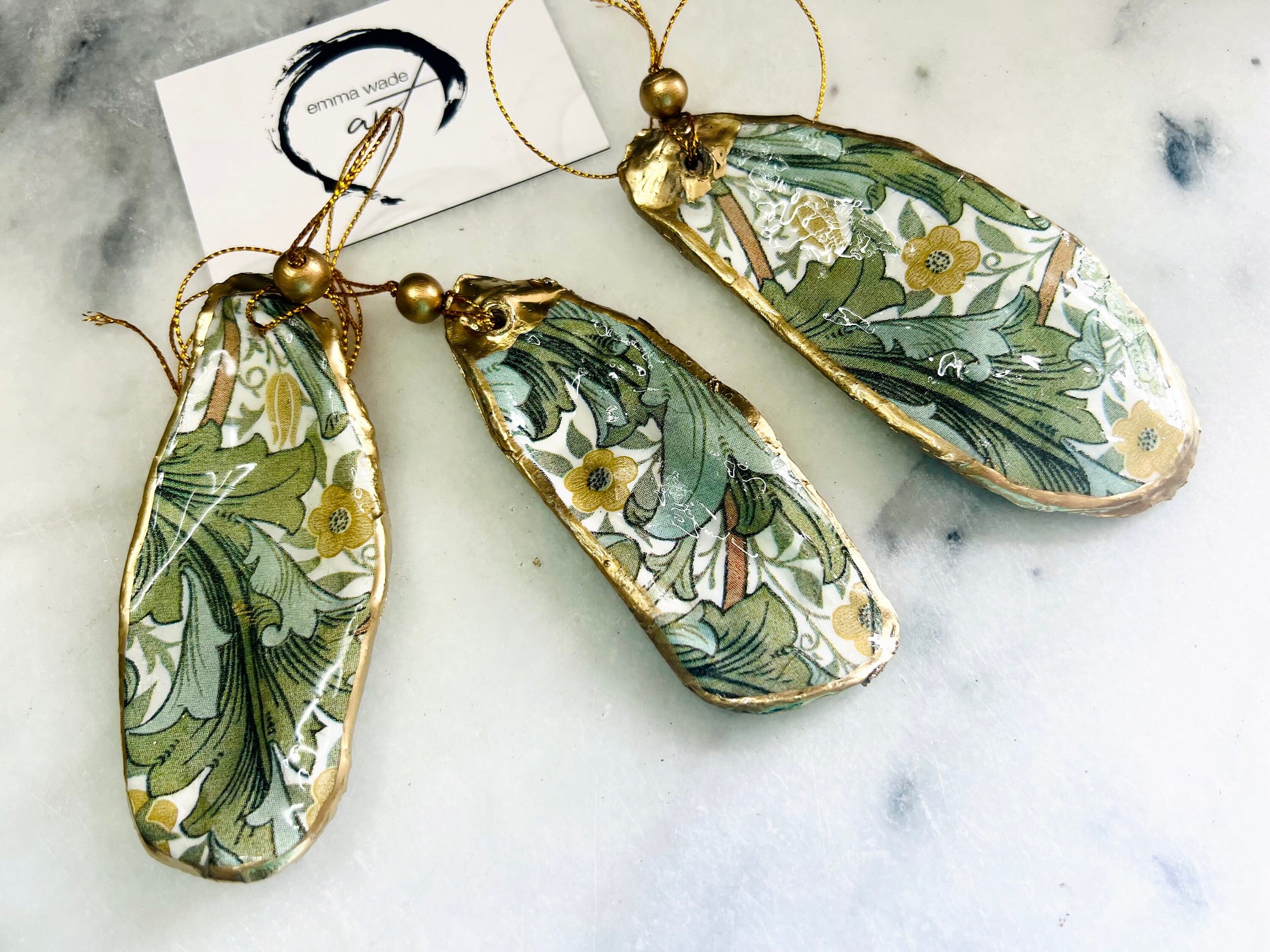 Handmade Dorset oyster shell hanging ornaments featuring William Morris inspired Golden Lily and Granville floral designs in soft green, blush pink and gold tones. Natural oyster shells finished with liquid gold leaf edging and sealed in glossy resin. Decorative hanging ornaments with gold cord and bead detail, suitable for luxury Christmas décor, coastal interiors, cottagecore styling or elegant year-round home decoration.