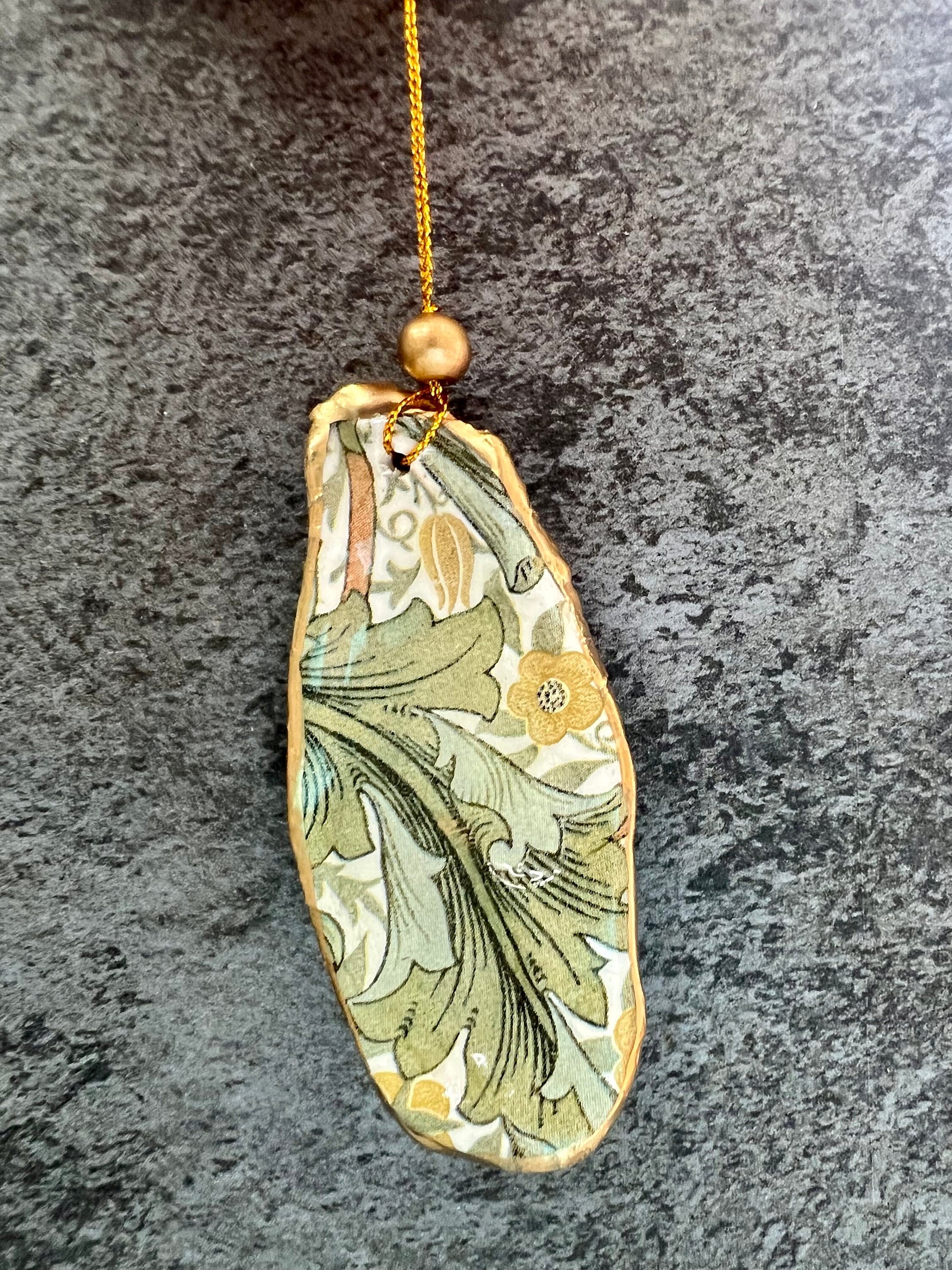 Handmade Dorset oyster shell hanging ornaments featuring William Morris inspired Golden Lily and Granville floral designs in soft green, blush pink and gold tones. Natural oyster shells finished with liquid gold leaf edging and sealed in glossy resin. Decorative hanging ornaments with gold cord and bead detail, suitable for luxury Christmas décor, coastal interiors, cottagecore styling or elegant year-round home decoration.